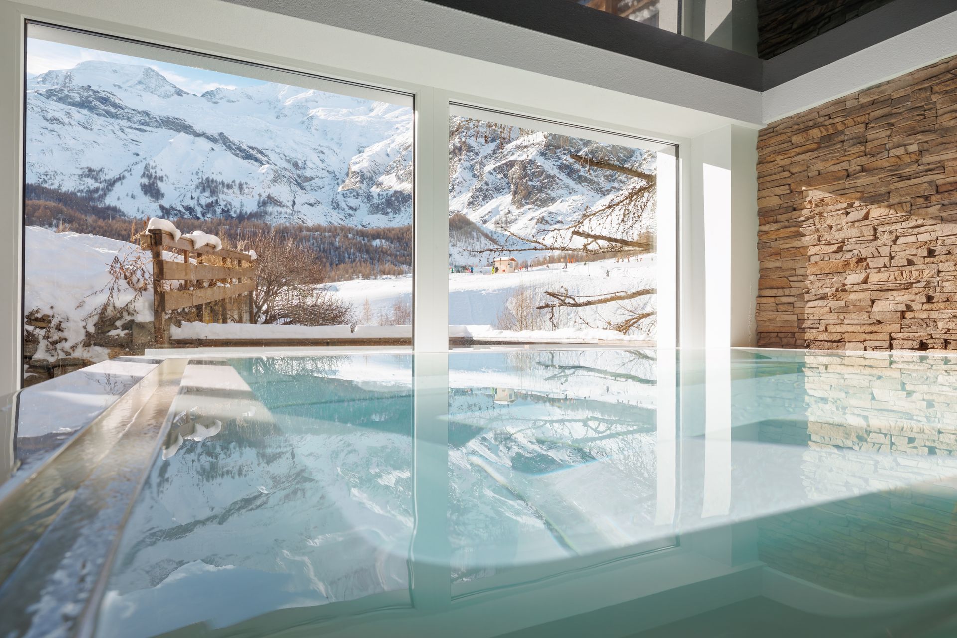 Indoor hot spring pool with floor-to-ceiling windows overlooking snowy mountains