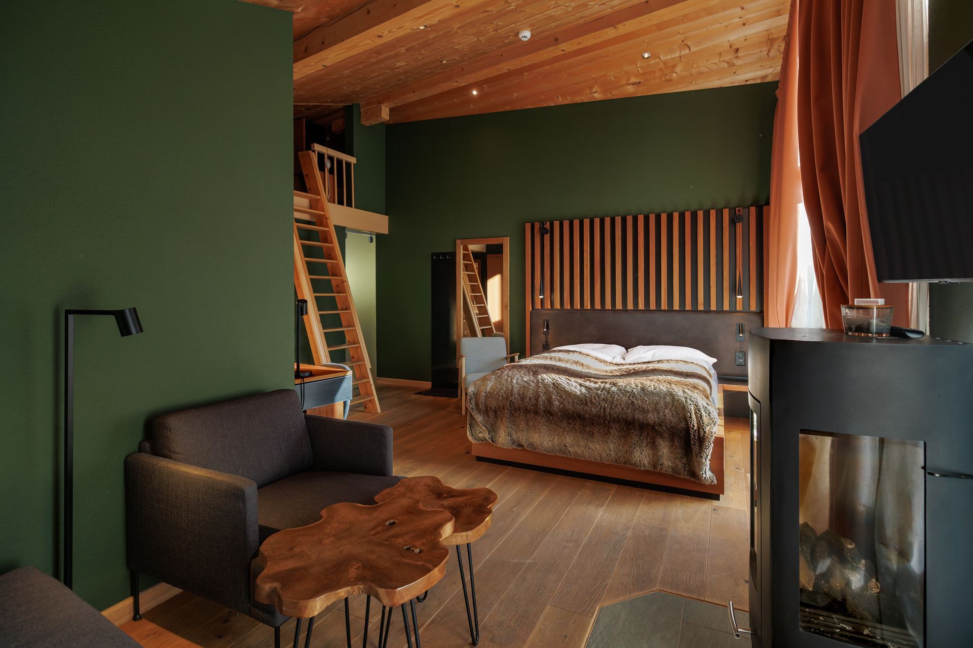 Cozy modern bedroom with wood ceiling, green walls, bed, sofa, and fireplace.