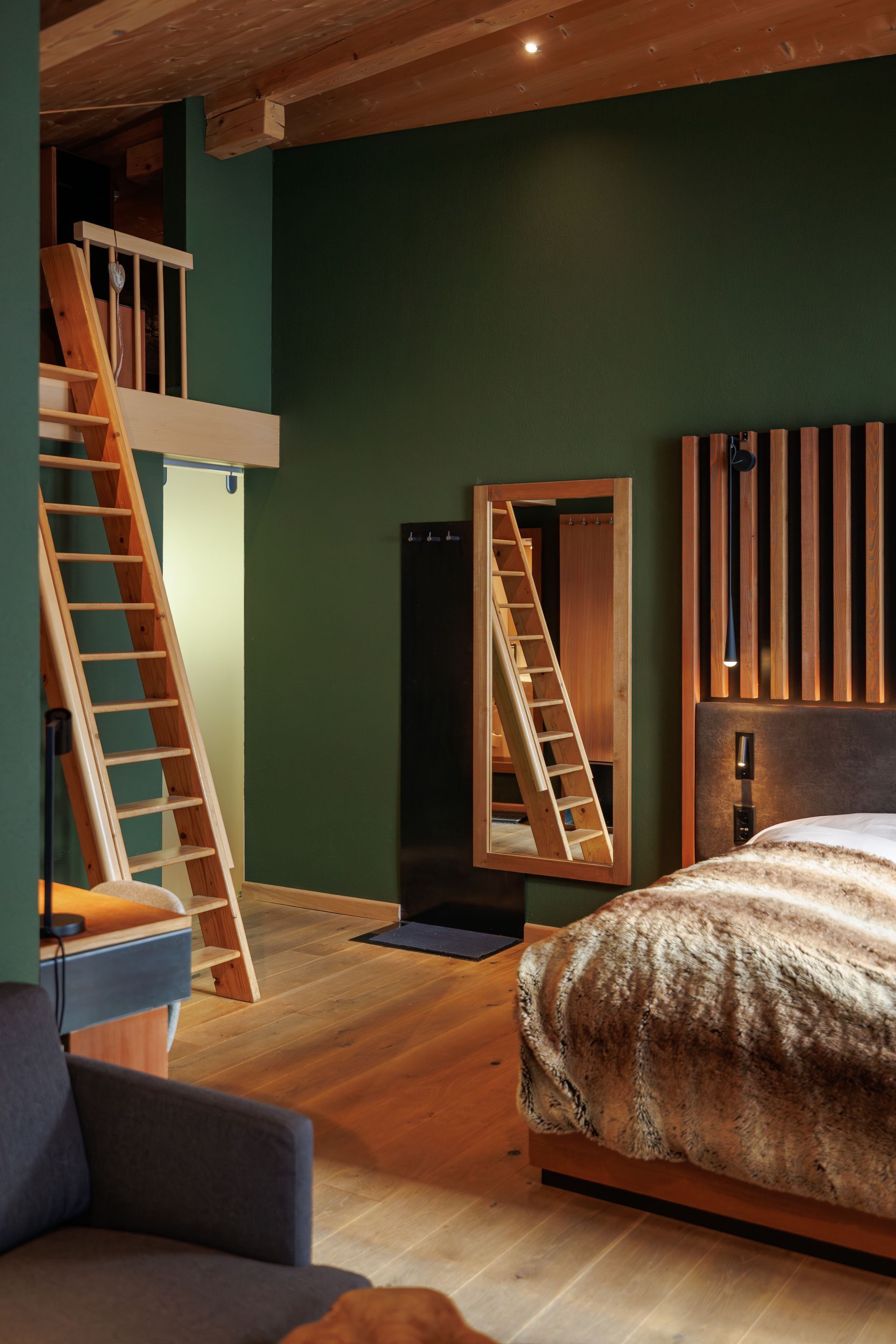 Modern bedroom with green wall, wooden bed, mirrored door, and two ladders leaning against the loft area