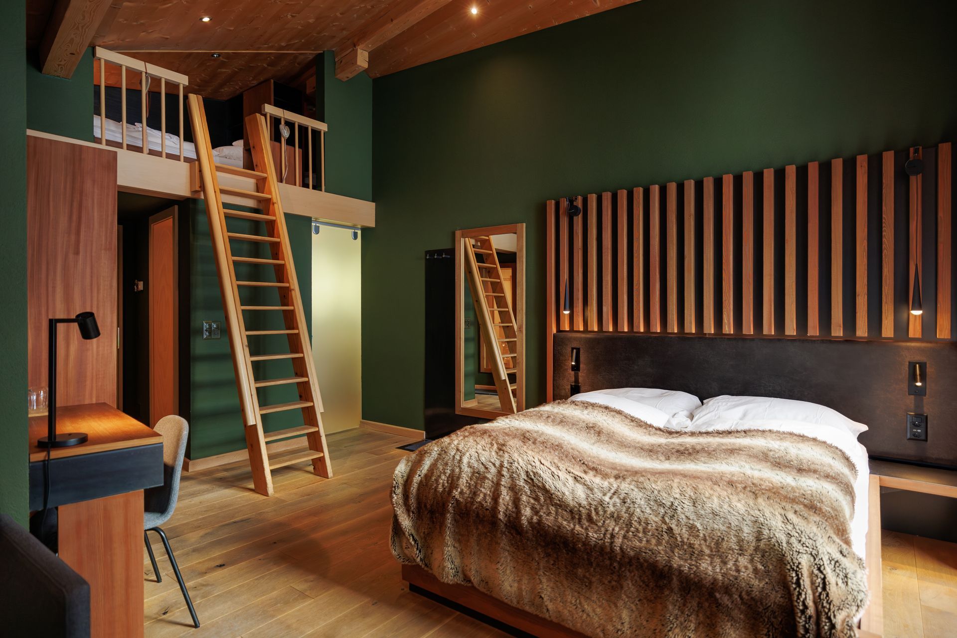 Loft bedroom with ladder, wood ceiling, green walls, striped headboard, and bed with fur throw.