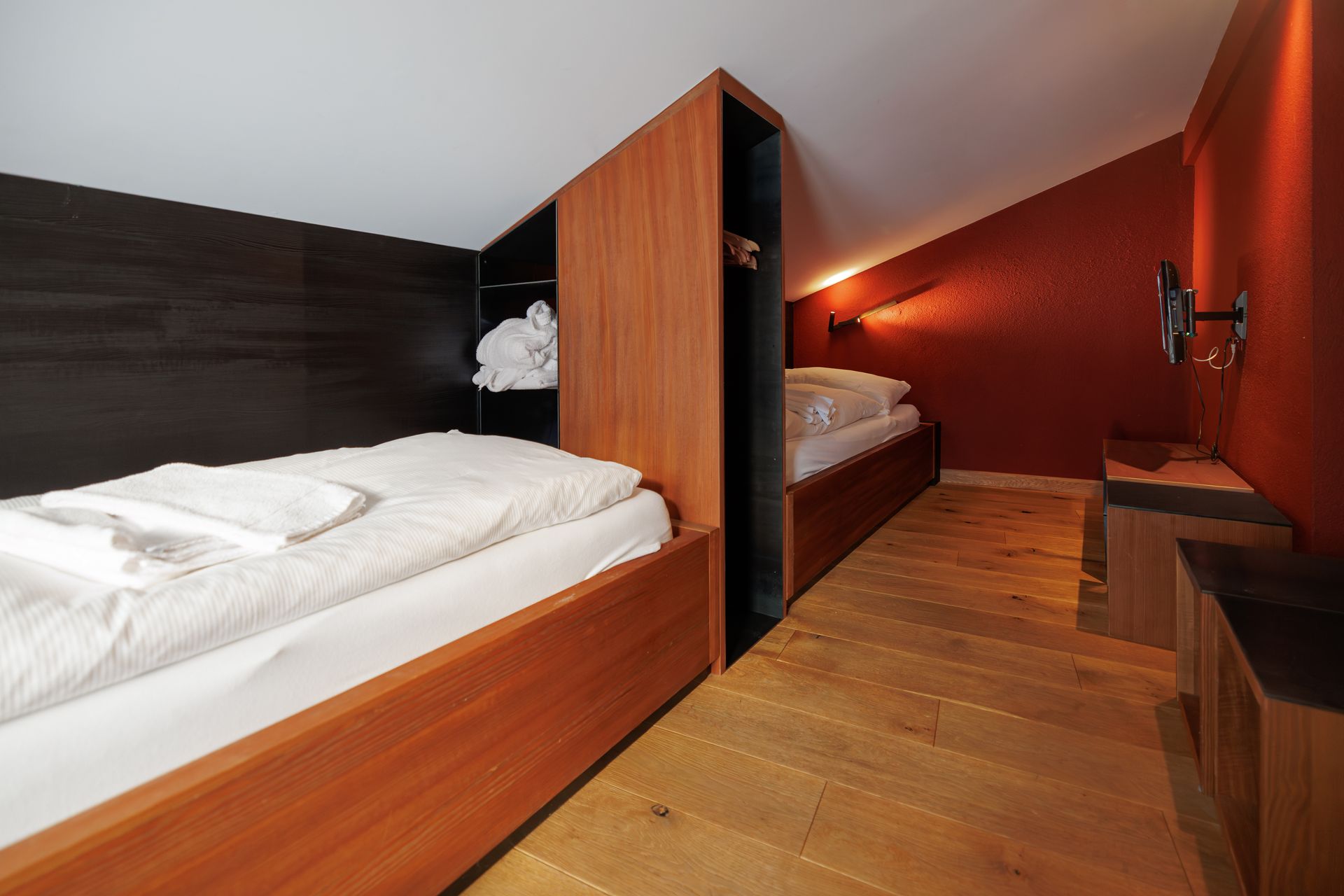 Two beds in a modern wood-paneled hotel room with red walls and a wooden floor.