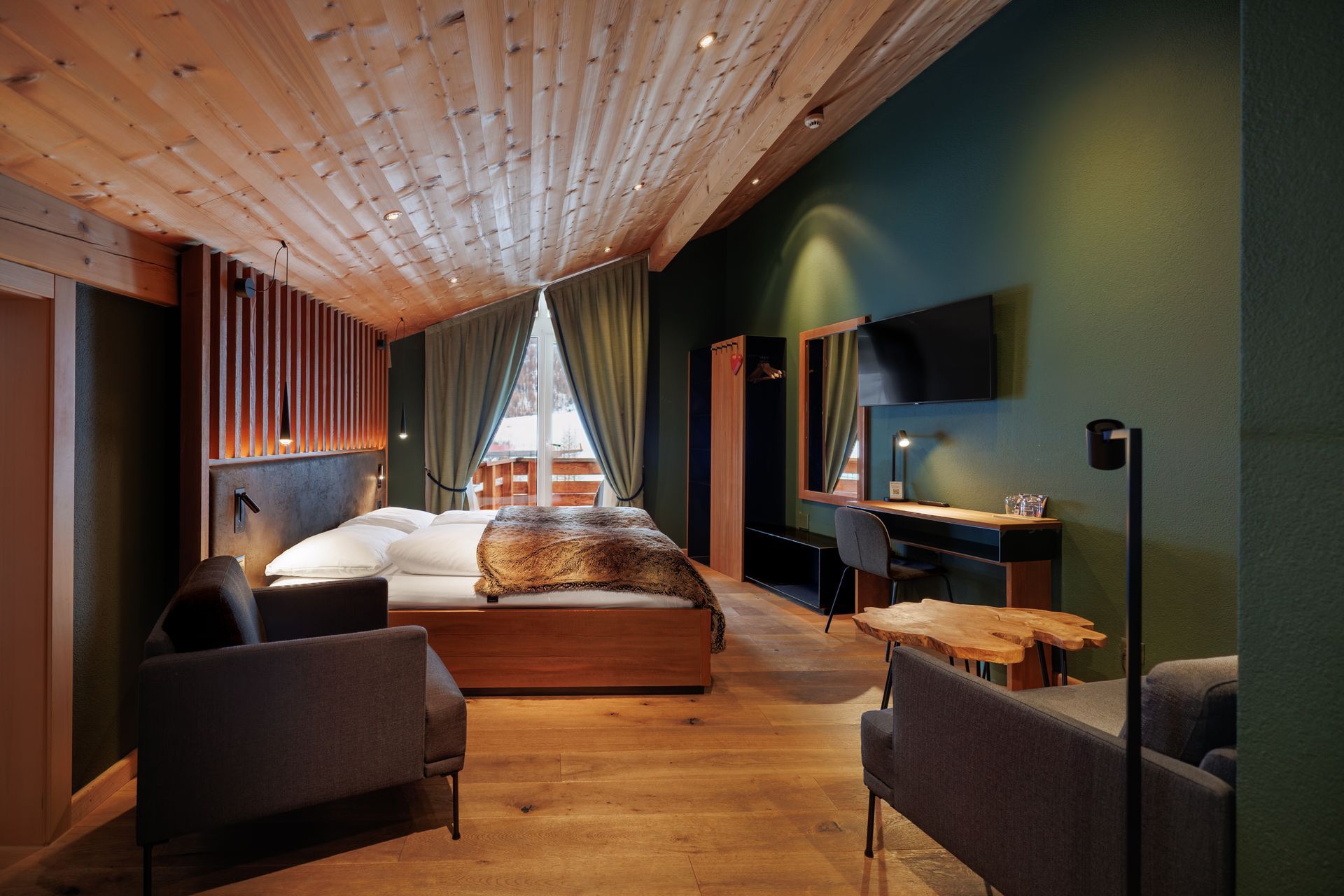 Modern hotel bedroom with wooden ceiling, canopy bed, and dark green walls, warmly lit by curtains and lamps