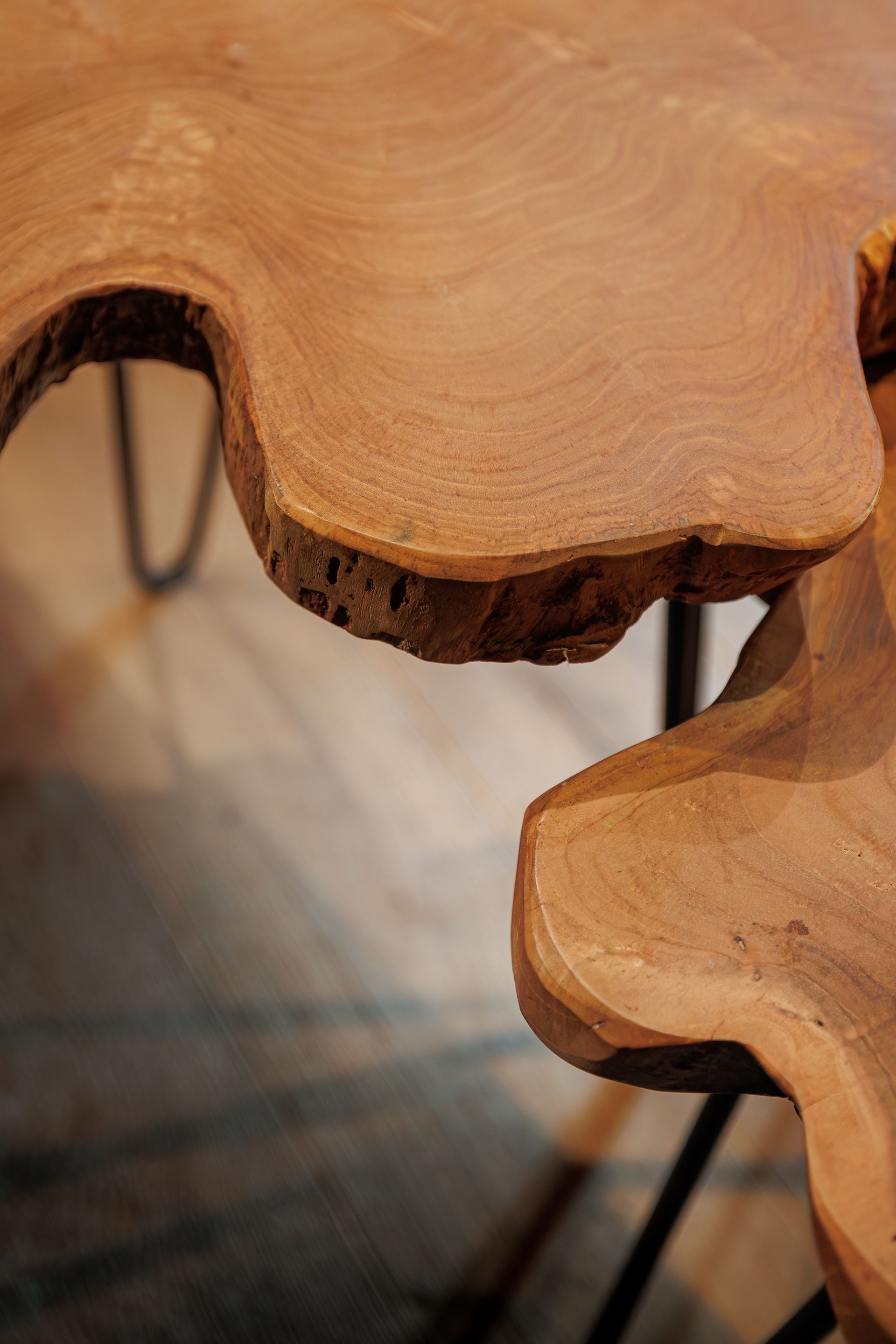 Close-up of a wooden table edge with natural live edges and metal legs underneath
