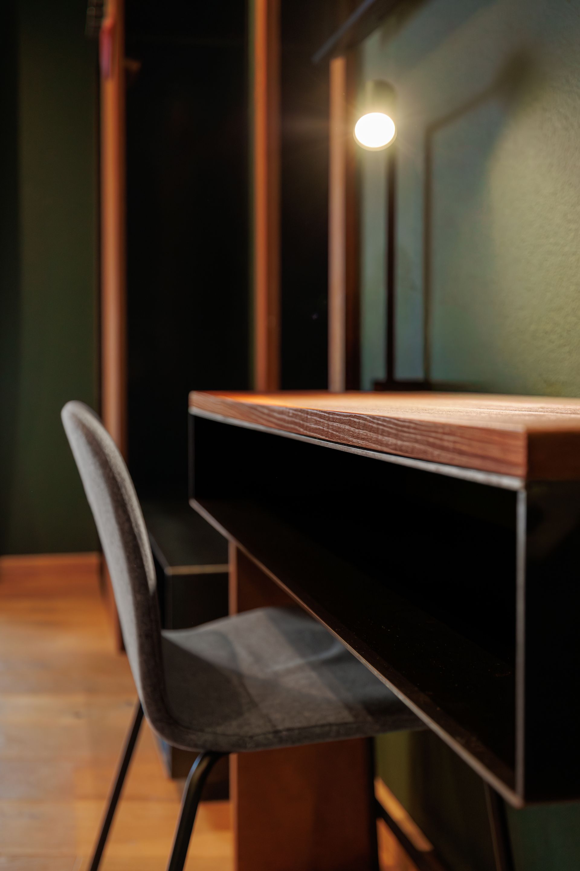 Modern desk with gray chair in a dimly lit room, beside a glowing wall lamp