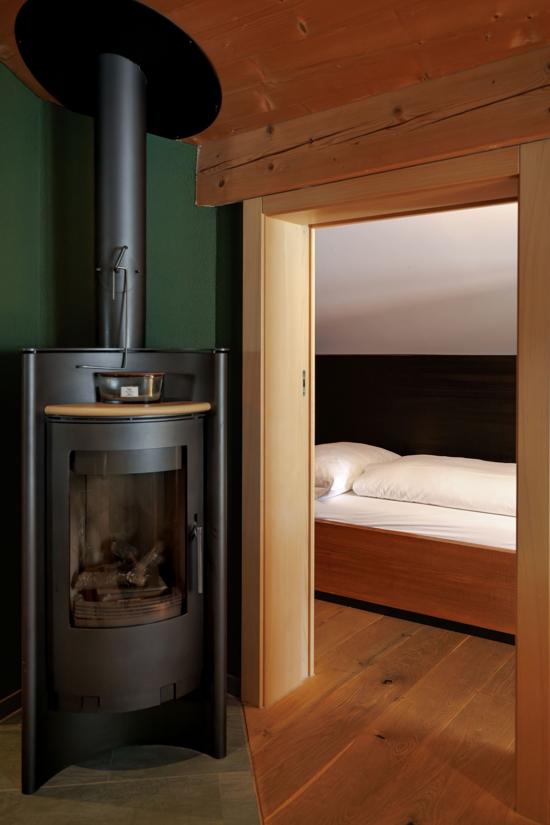 Cozy wooden room with a black wood stove beside an open doorway to a bed alcove