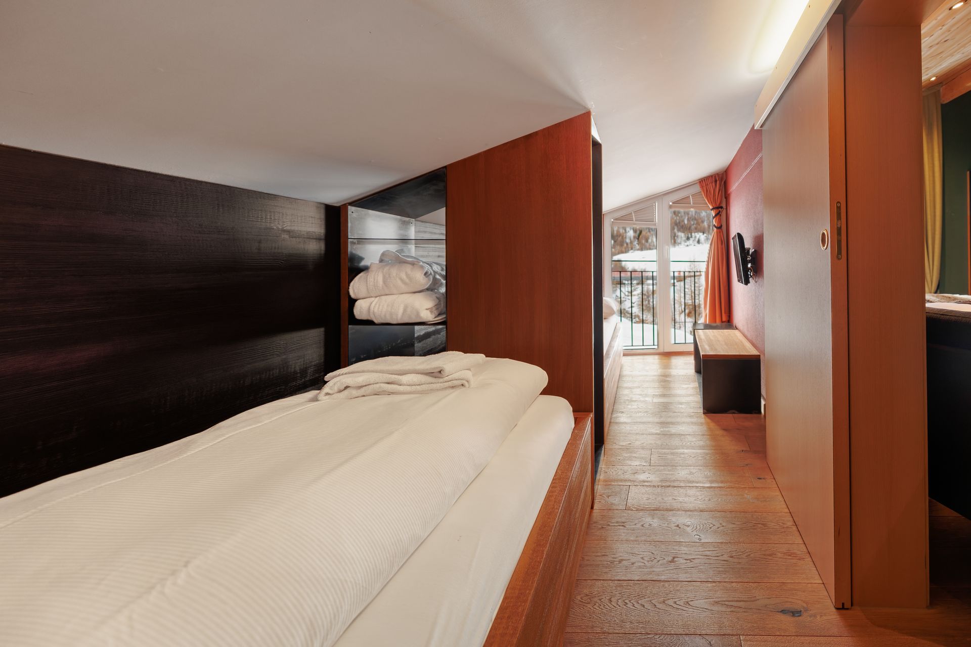Modern bedroom with a low bed, wood paneling, and a windowed seating area at the far end