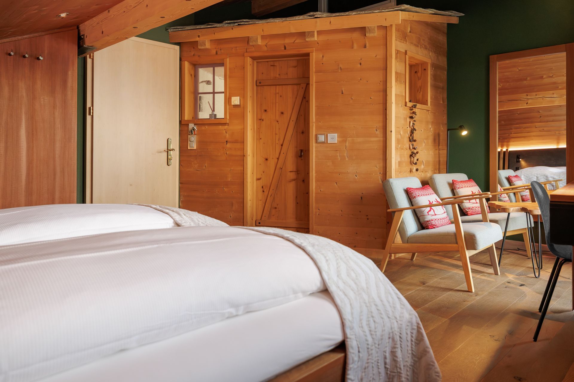 Cozy wooden cabin bedroom with two white beds, a small sitting area, and warm natural light