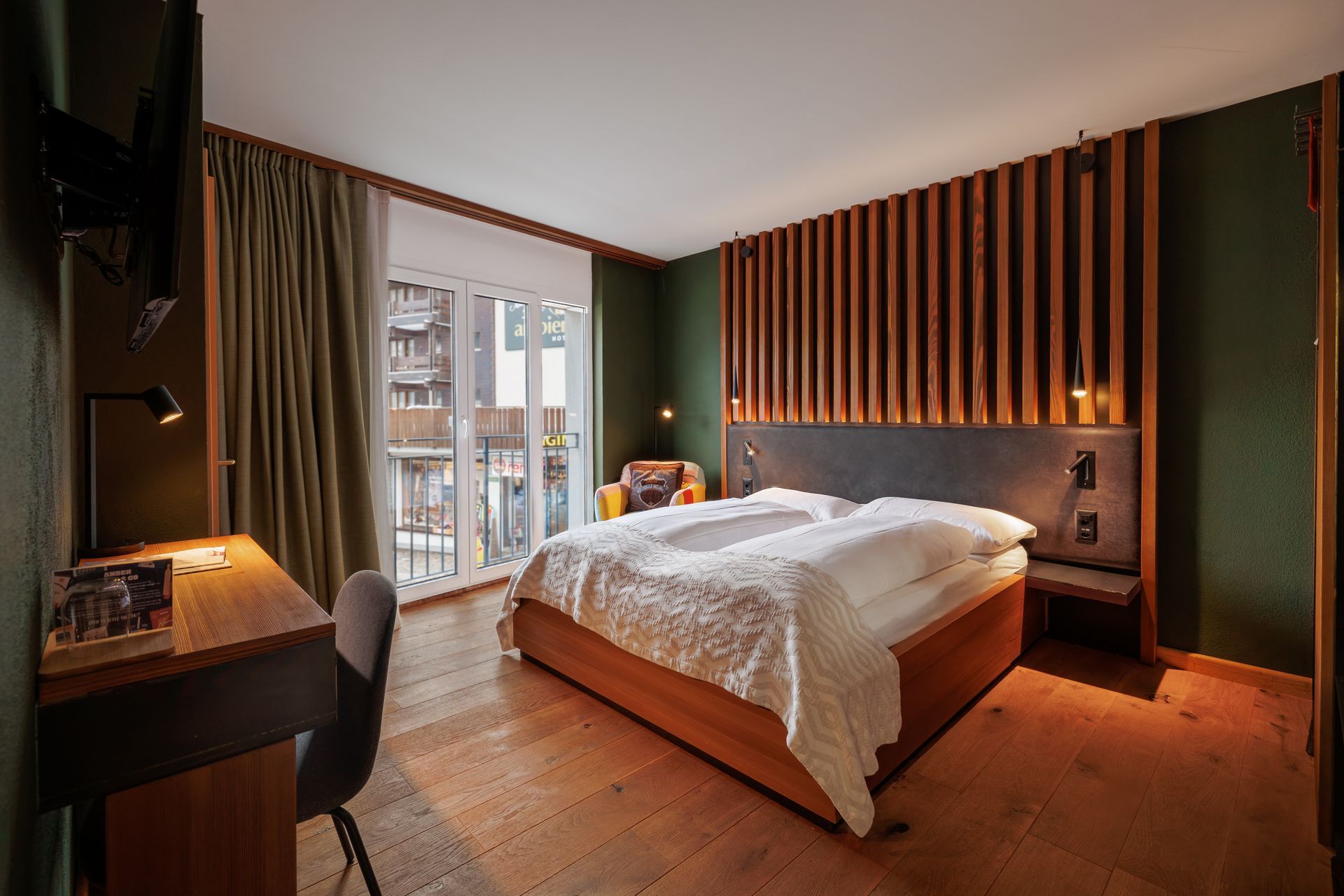 Modern bedroom with a bed, desk, warm lighting, and floor-to-ceiling windows with curtains