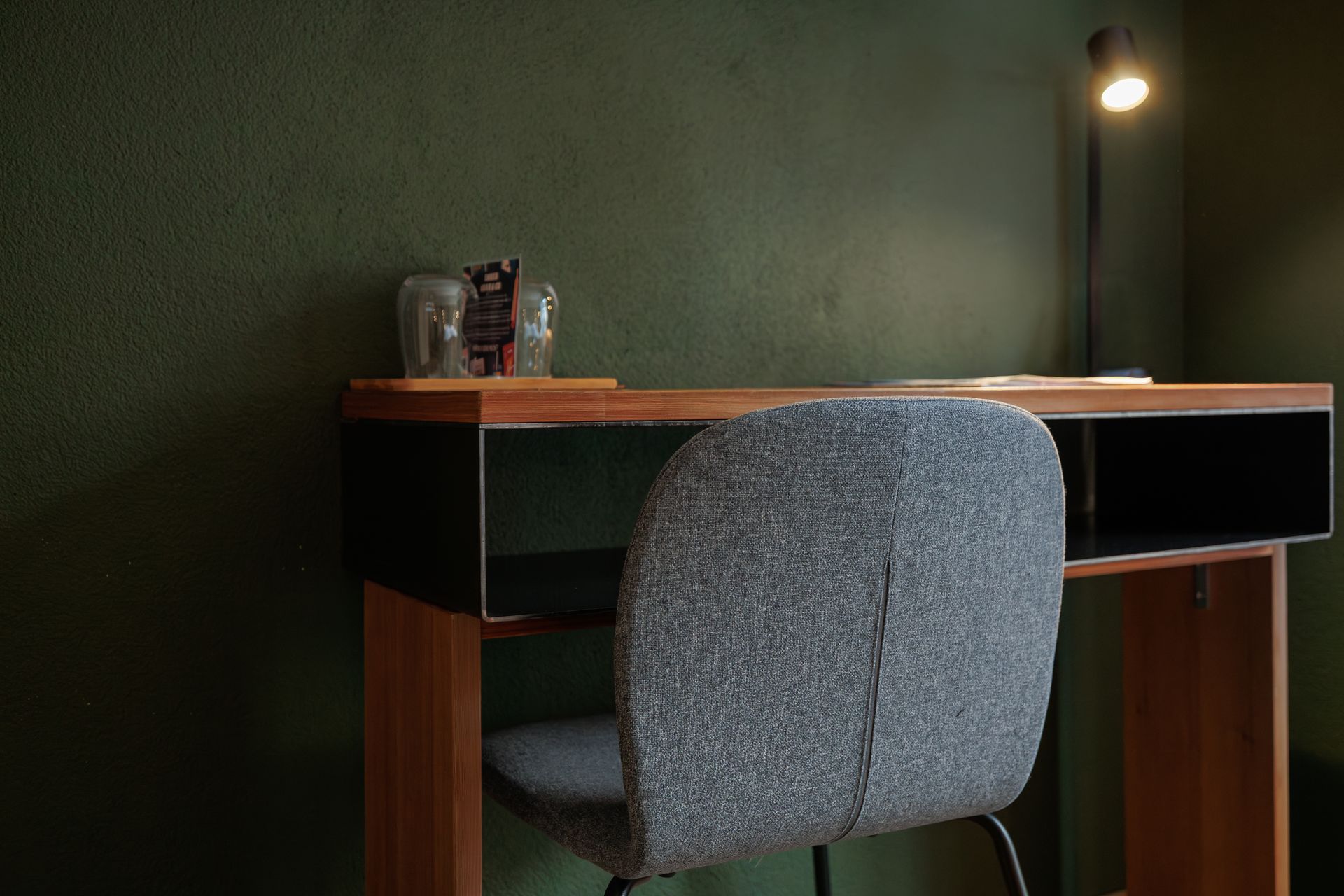 Gray chair at a wooden desk with a lit lamp in a dim room