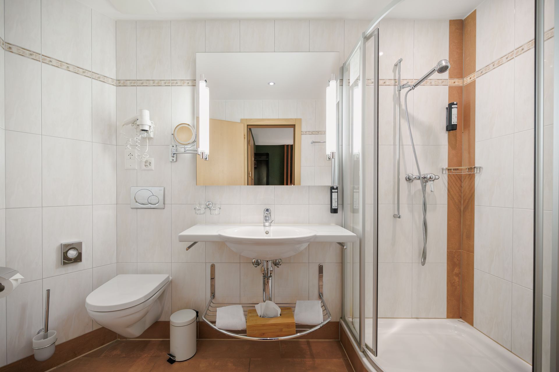 Bright tiled bathroom with toilet, sink, mirror, and shower stall