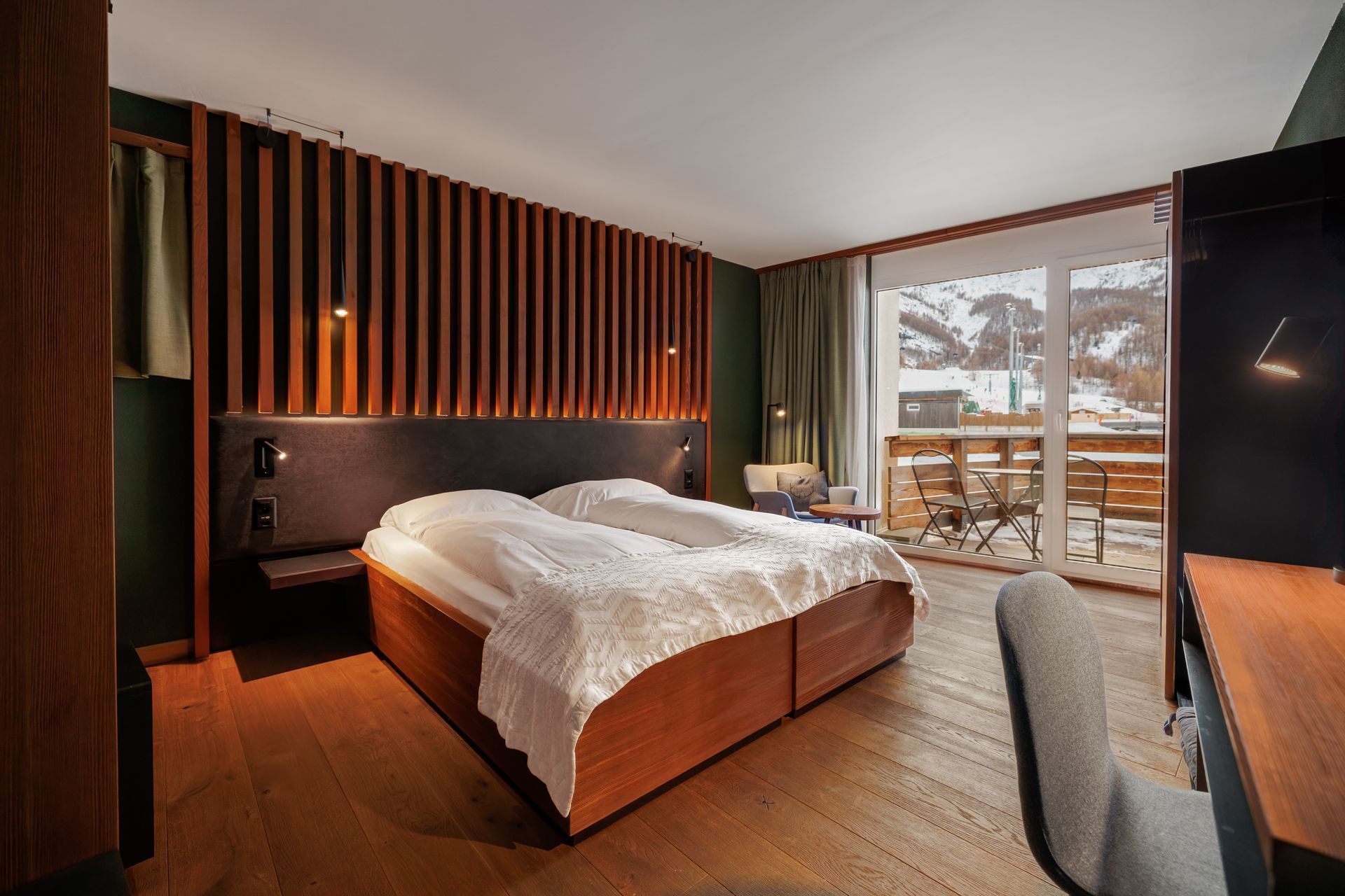 Modern bedroom with wood accents, a large bed, and a balcony view of snowy trees