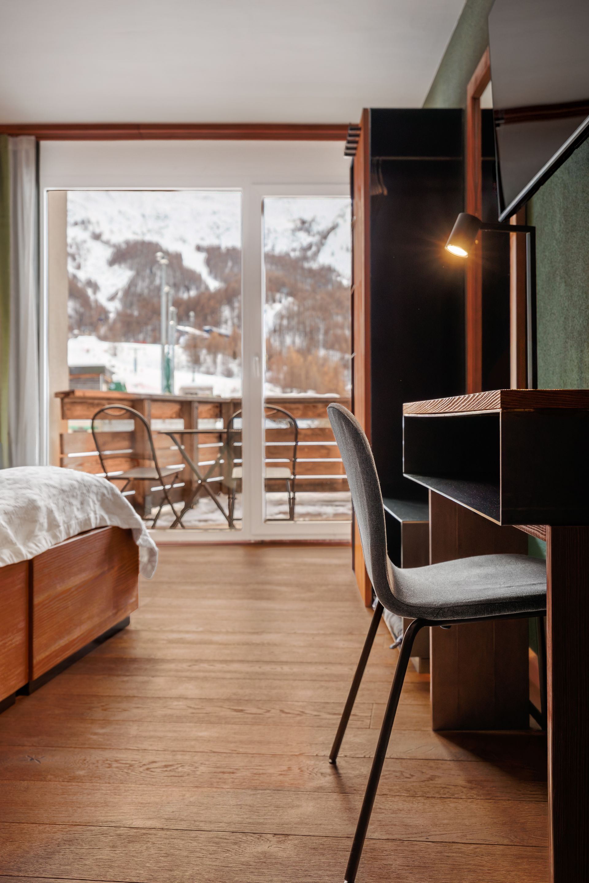 Cozy hotel room with a bed, desk chair, and balcony view of snowy mountains