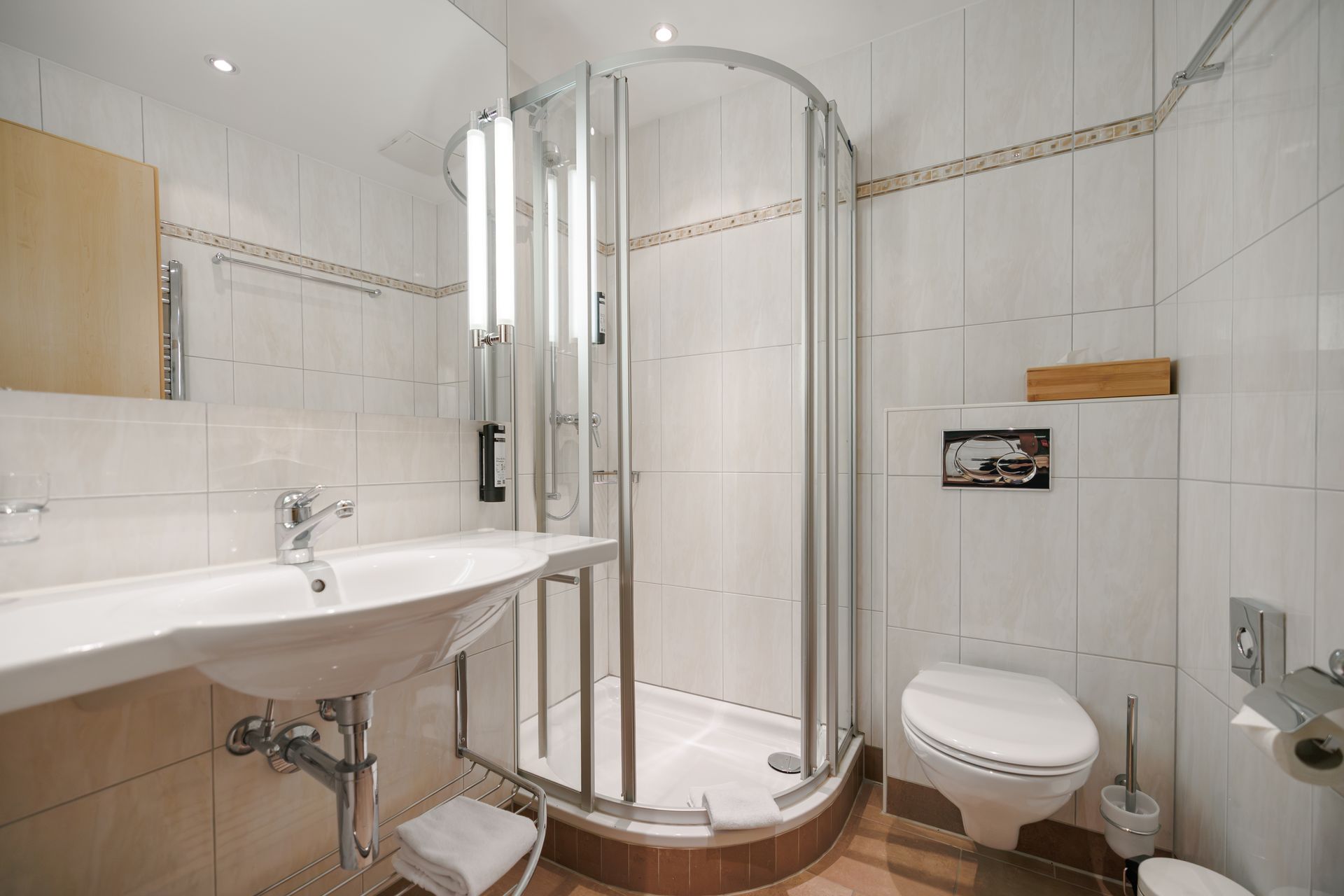 Compact white bathroom with sink, glass shower, and wall-mounted toilet