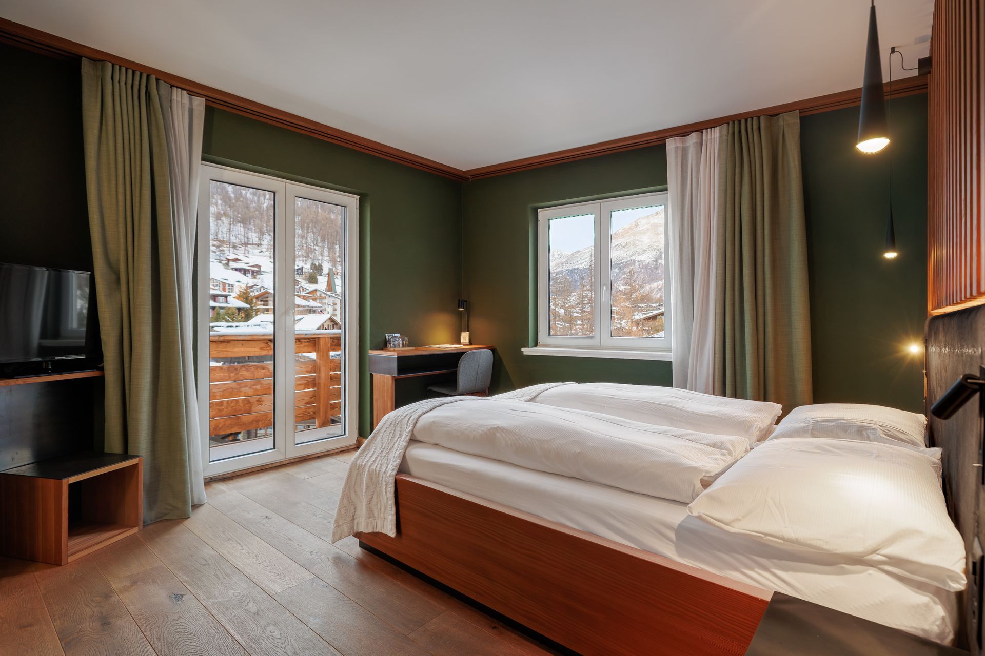 Cozy bedroom with a wooden bed, green walls, and windows overlooking snowy trees
