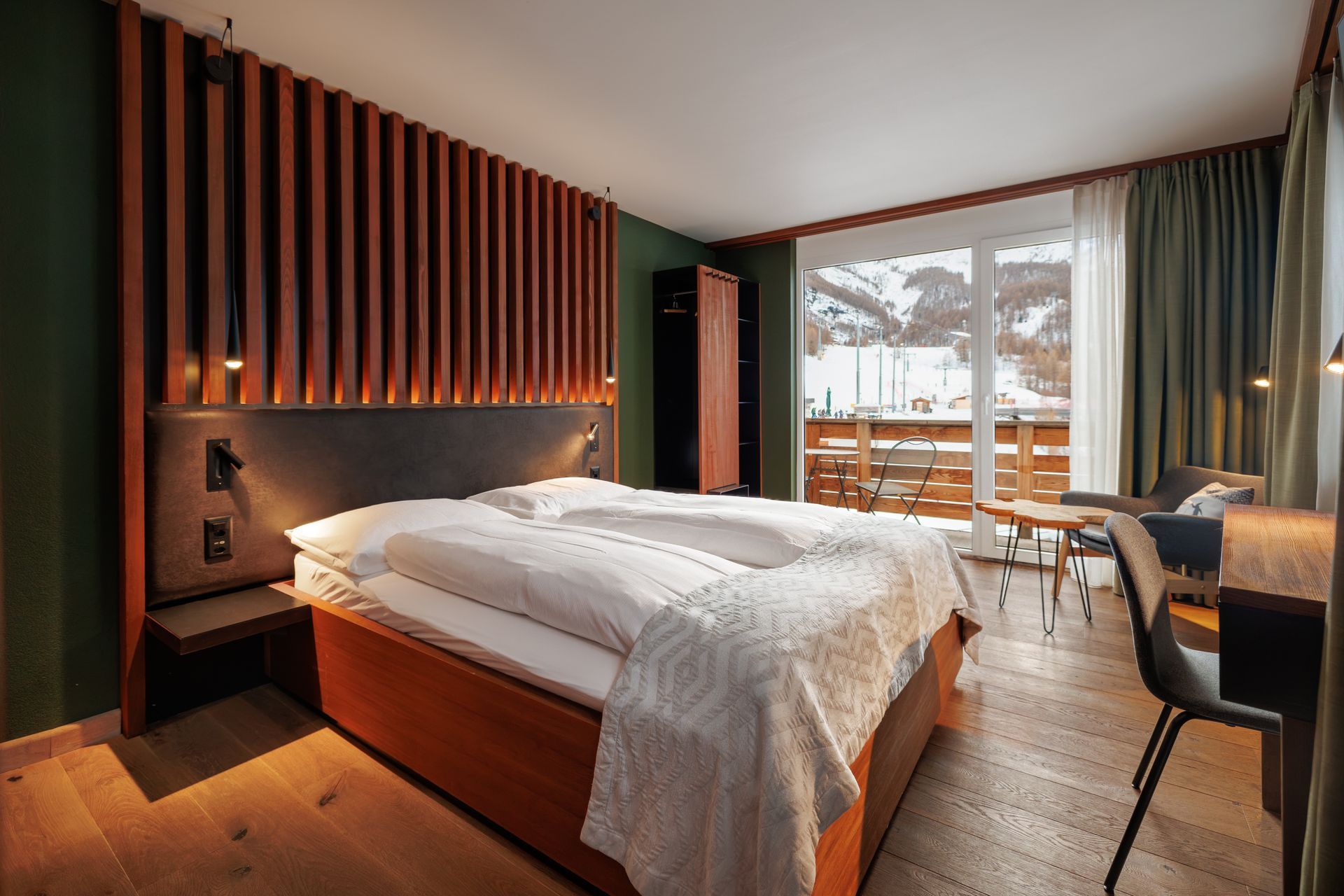 Modern bedroom with a large bed, warm wood paneling, and a balcony view through glass doors