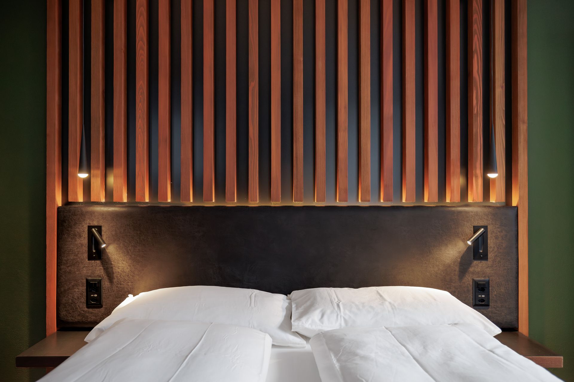 Modern hotel bed with white linens, dark headboard, and vertical wood slats on the wall