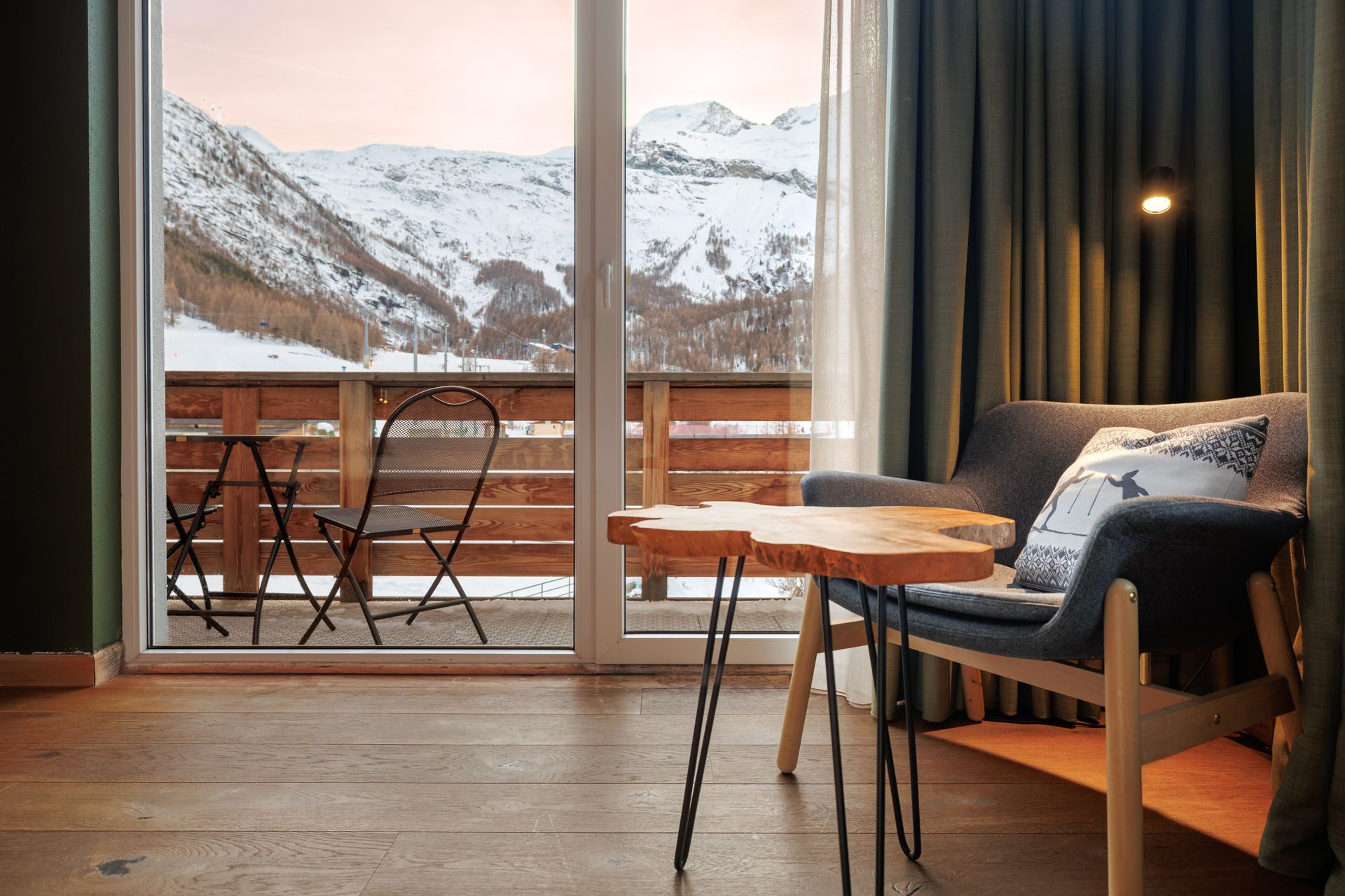 Cozy hotel room with balcony overlooking snowy mountains and a small table by the window