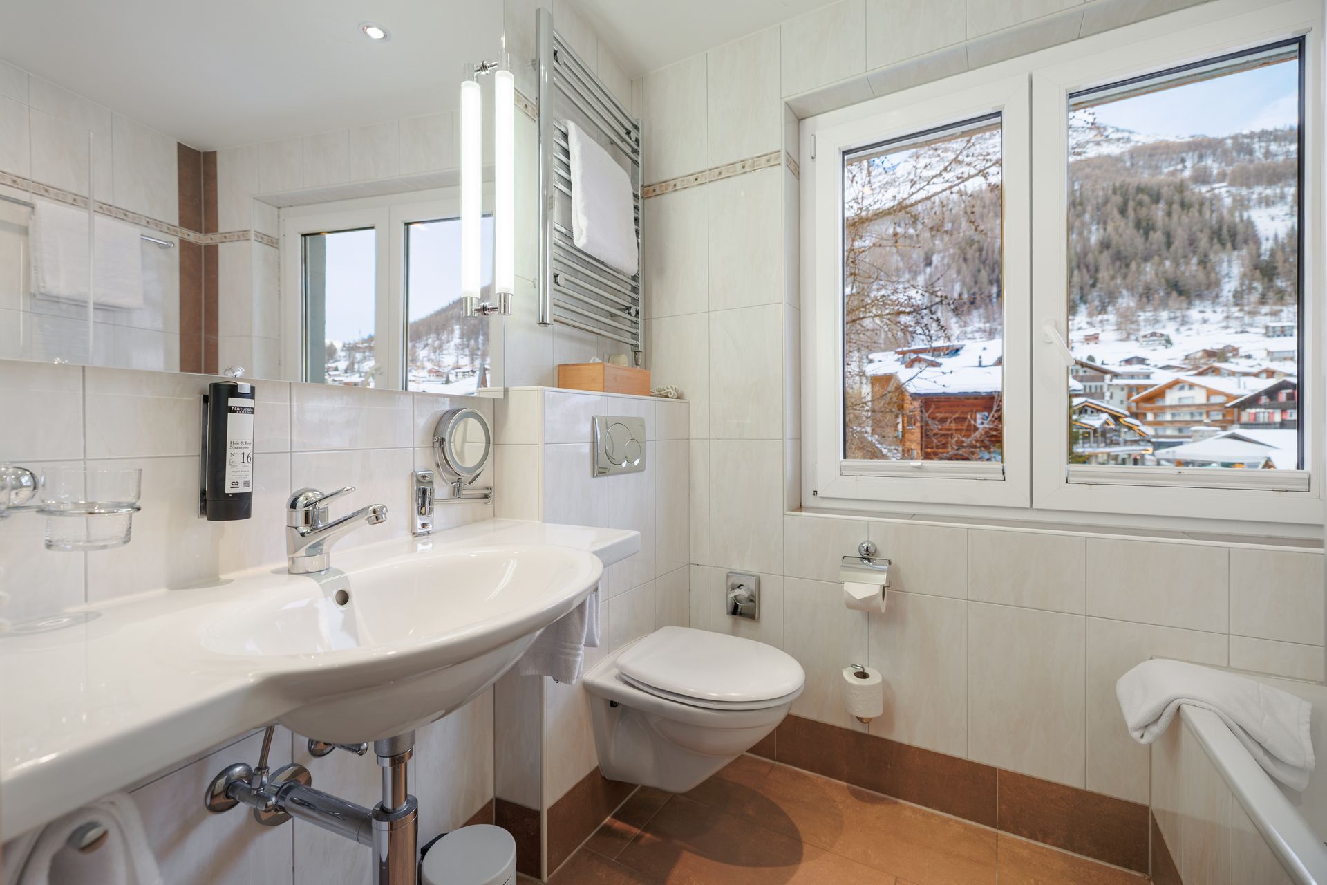 Bright bathroom with sink, toilet, and snowy mountain view through two windows