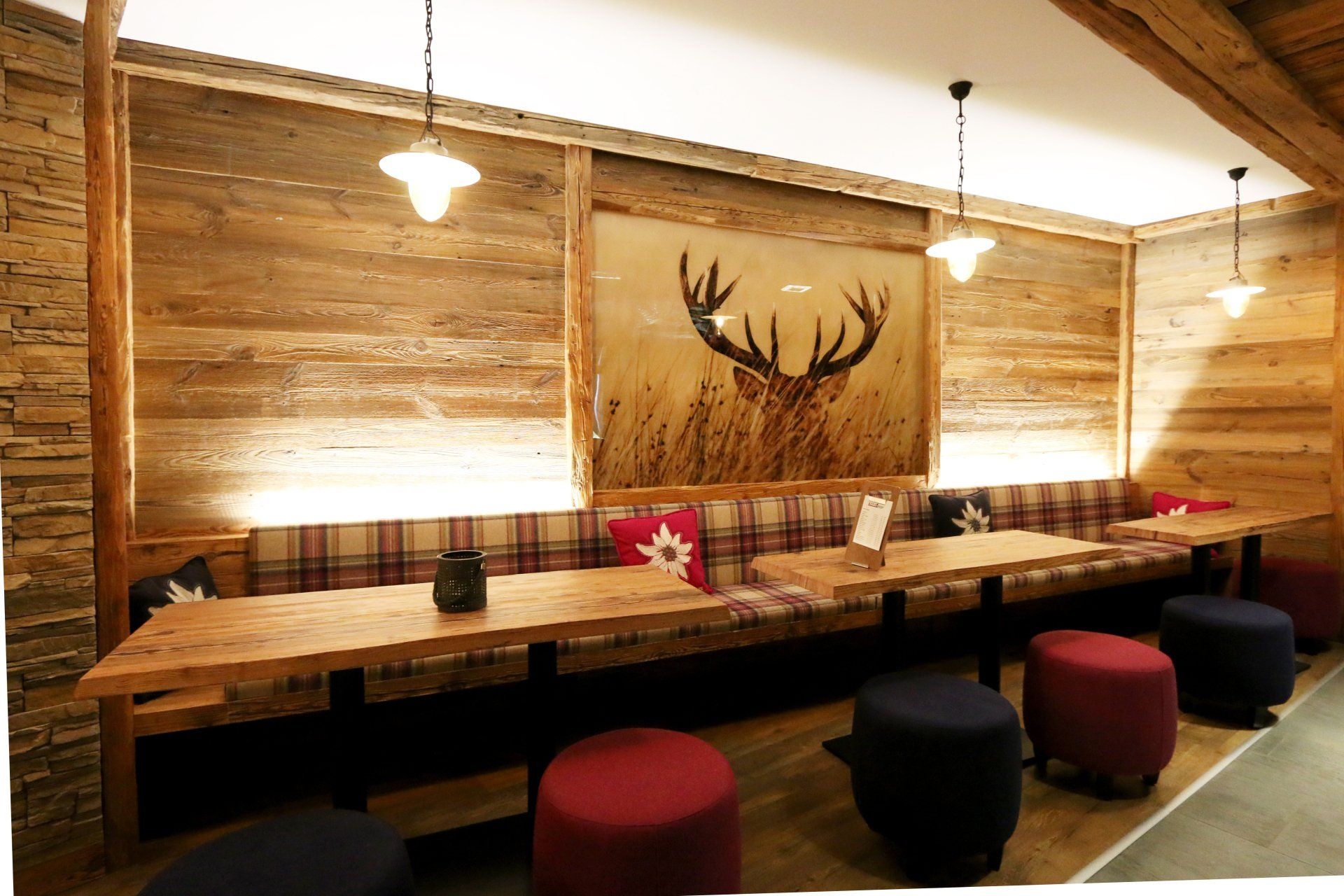 Rustic wooden dining room with a long table, red stools, and a deer antler wall hanging