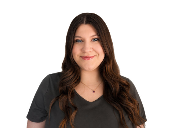 Person with long brown hair wearing a black V-neck shirt, smiling against a white background