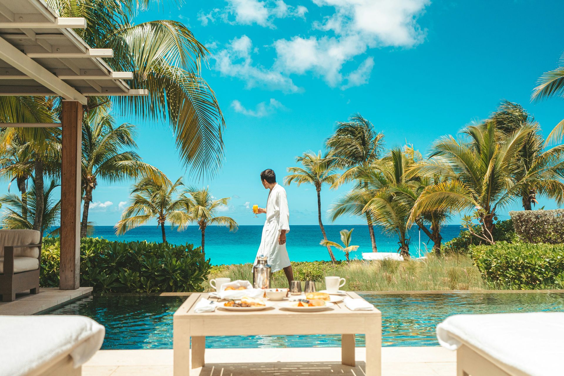 Beachfront resort patio with a person in white walking by palm trees and turquoise water
