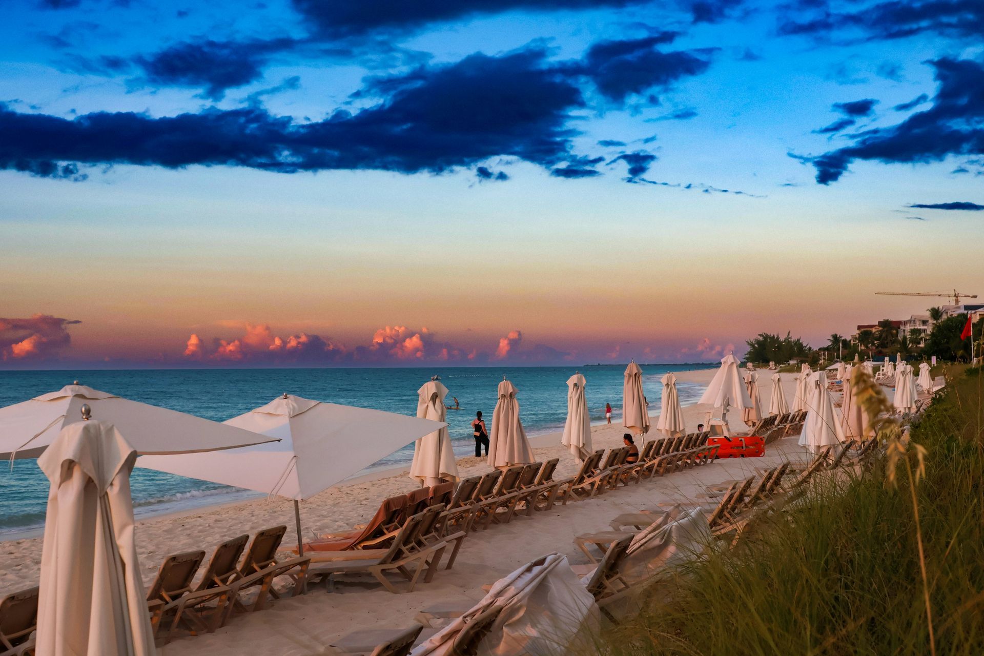 Beach loungers and closed white umbrellas at sunset by the ocean, with colorful clouds overhead