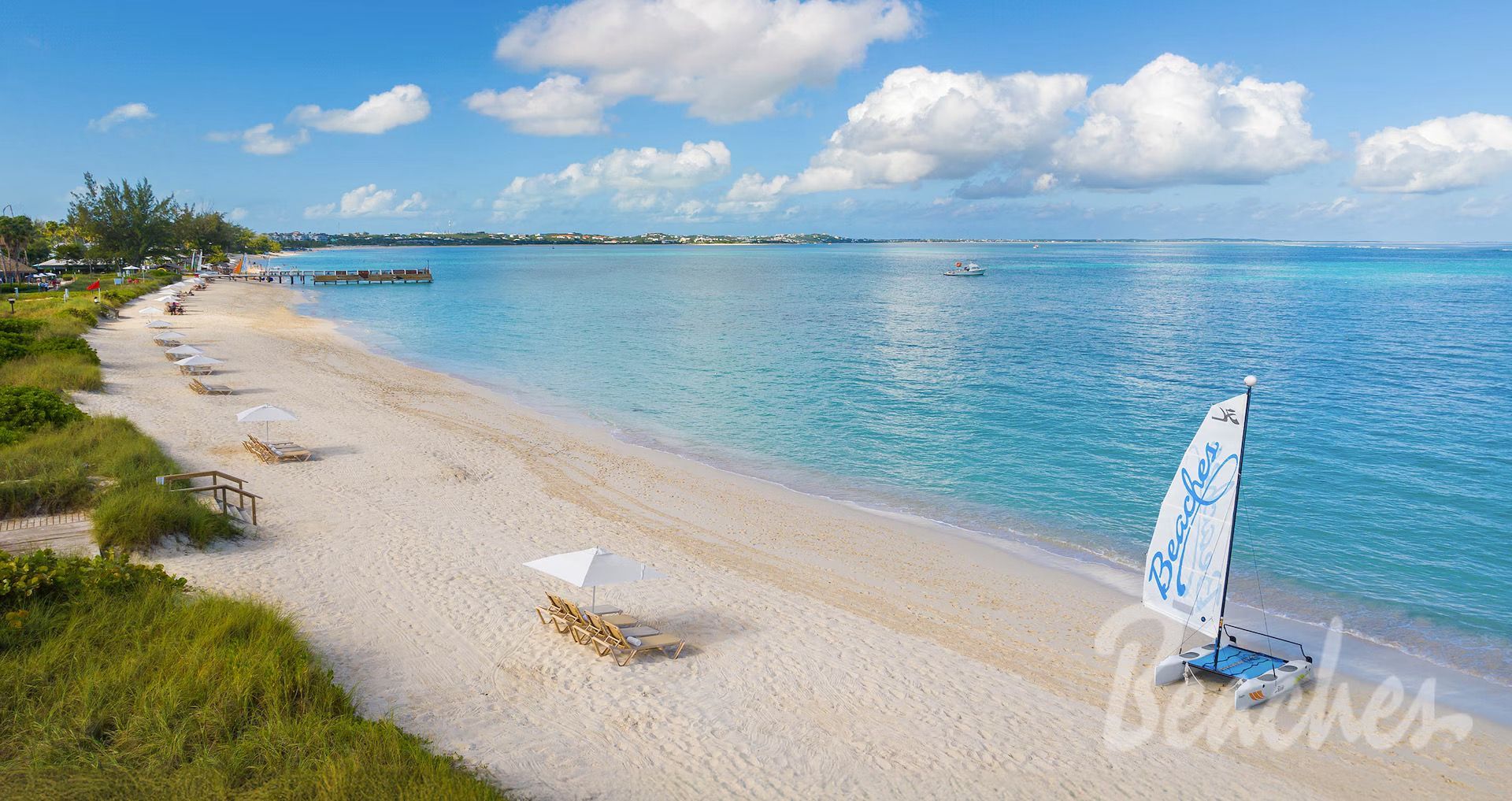 Sandy beach with turquoise water, blue sky, and a small white sailboat near shore