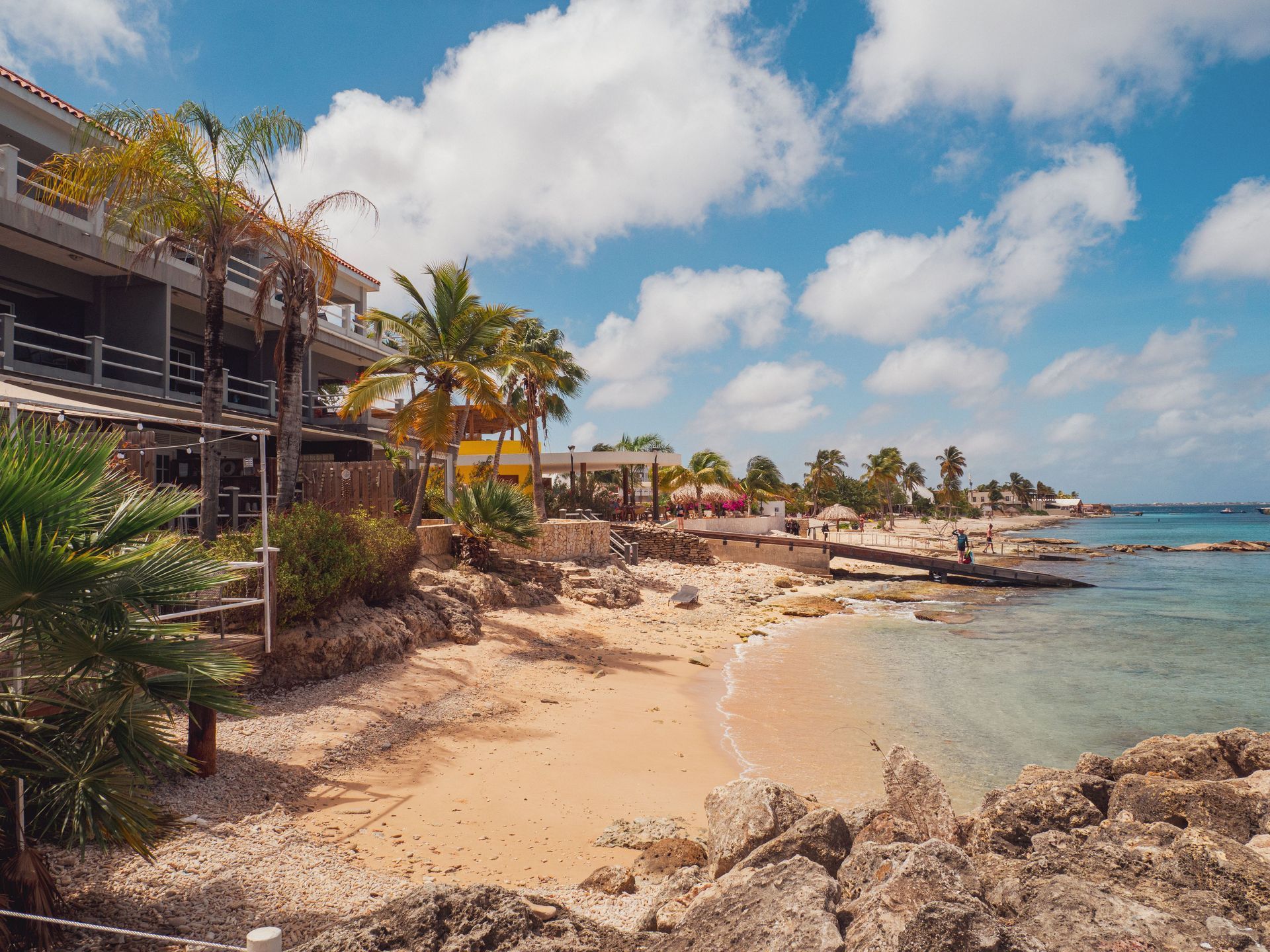 Sunny tropical beach with palm trees, sandy shore, and a seaside resort under a blue sky