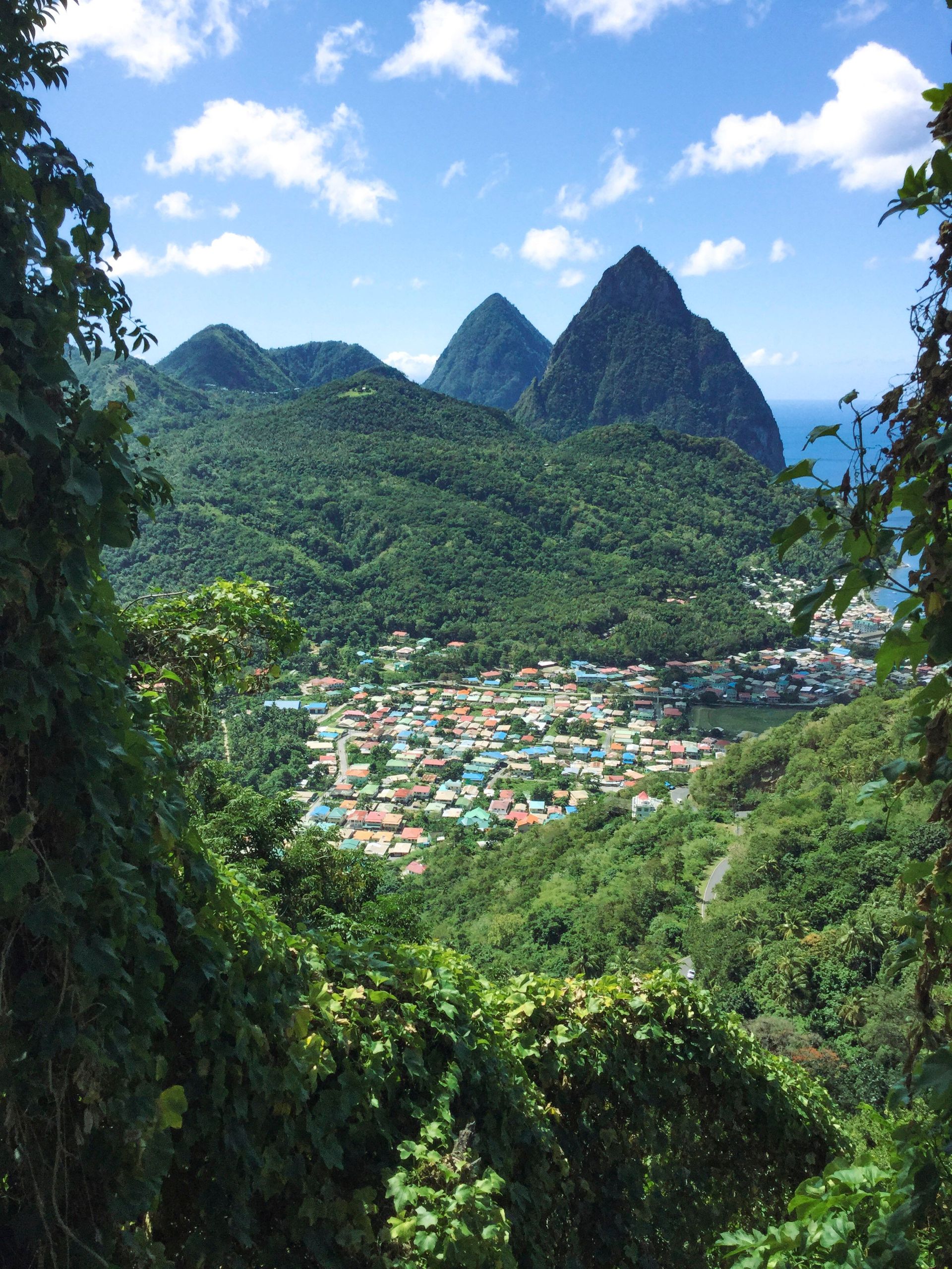 Tropical village nestled between lush green mountains under a bright blue sky with clouds
