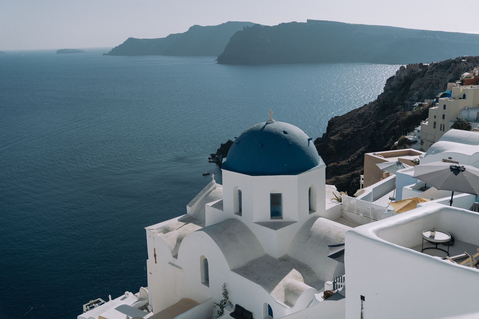 White cliffside buildings with a blue dome overlook the sea and distant islands at sunset.