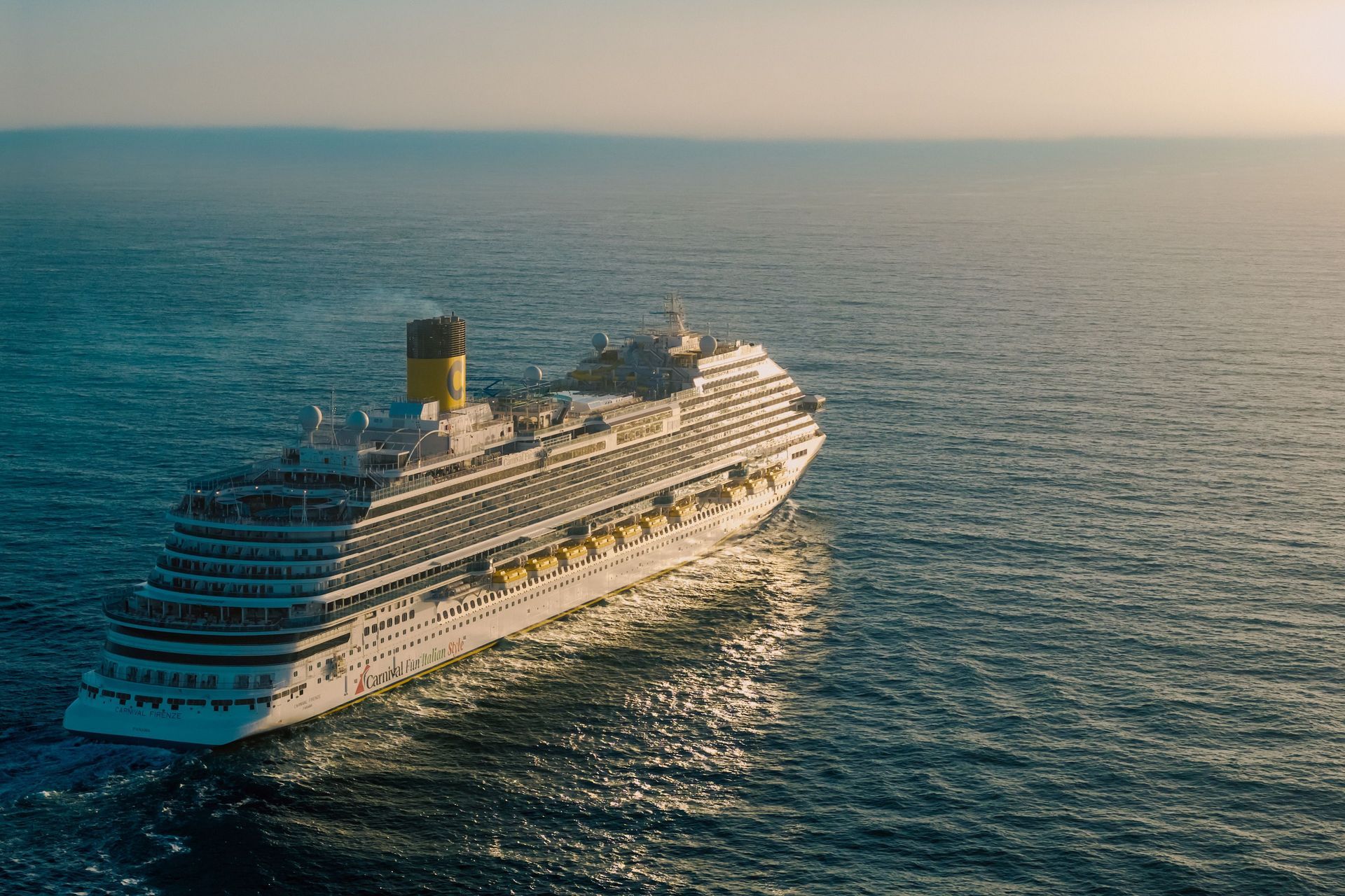 Large white cruise ship sailing on a calm blue ocean at sunset