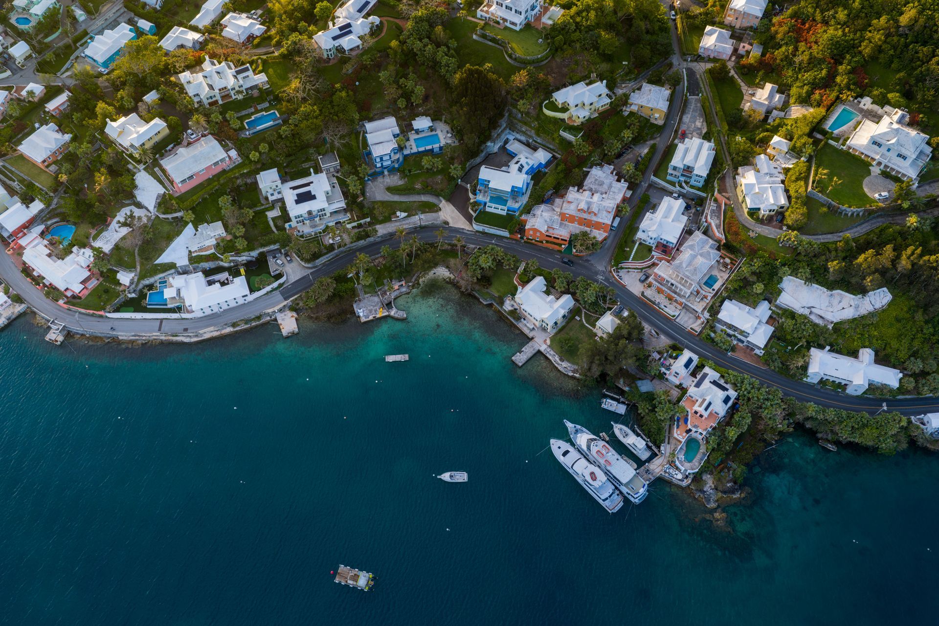 Aerial view of a tropical seaside resort with white-roofed buildings, dense greenery, and turquoise water with boats