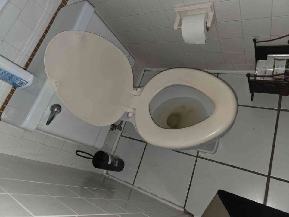 Open toilet with beige seat in a small tiled bathroom, seen from above.