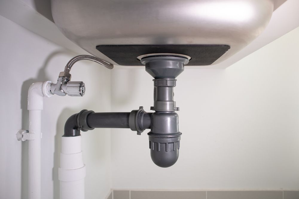 Under-sink plumbing with white drain pipes and a gray trap beneath a sink basin