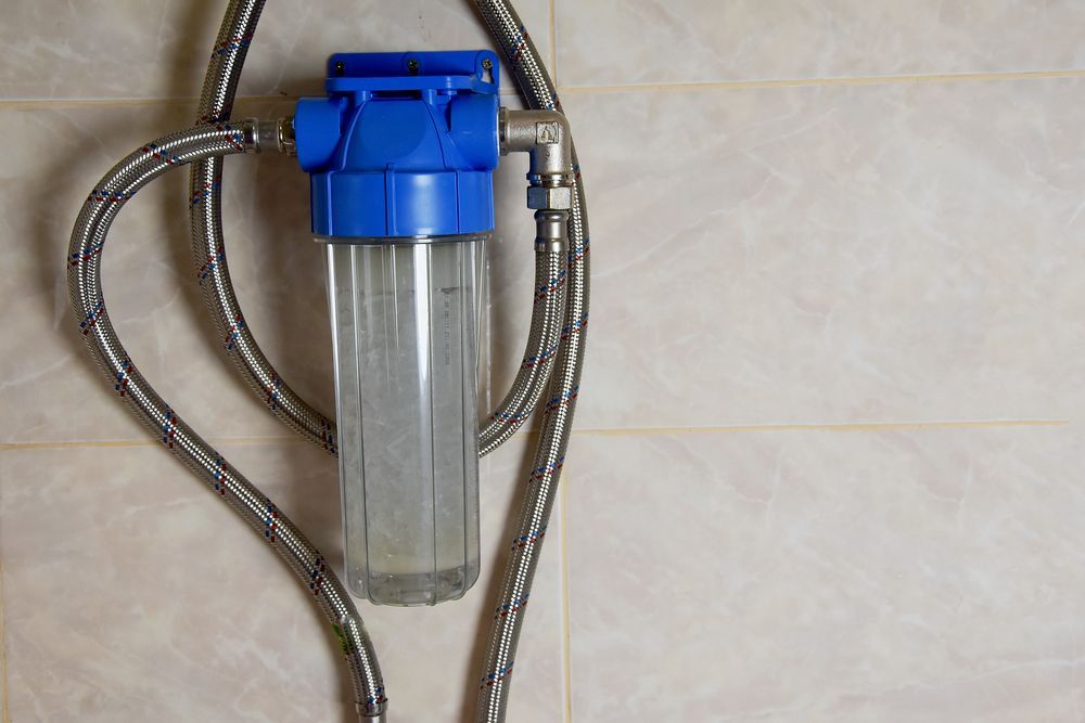Blue water filter mounted on a tiled wall with braided hoses attached