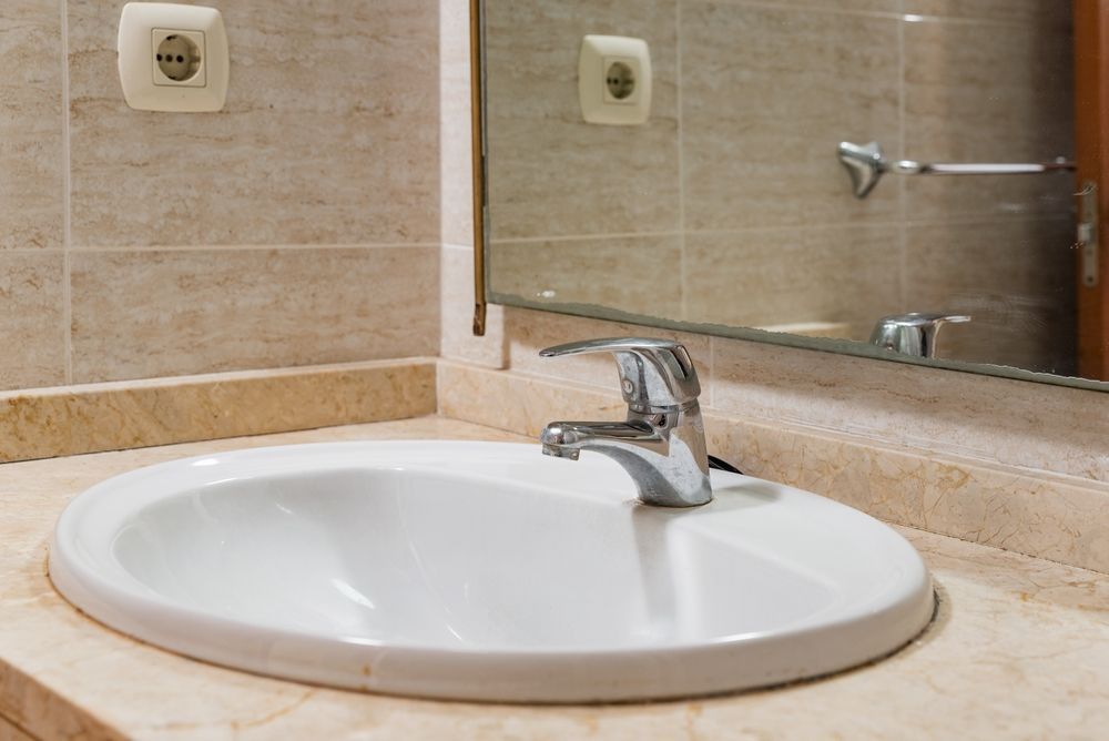 Bathroom sink with chrome faucet, white basin, beige tile countertop, and wall mirror