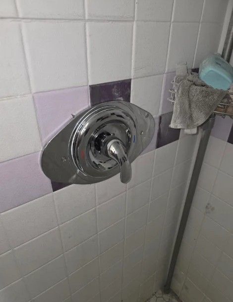 Chrome shower control knob on white and lavender tiled bathroom wall, with towel nearby