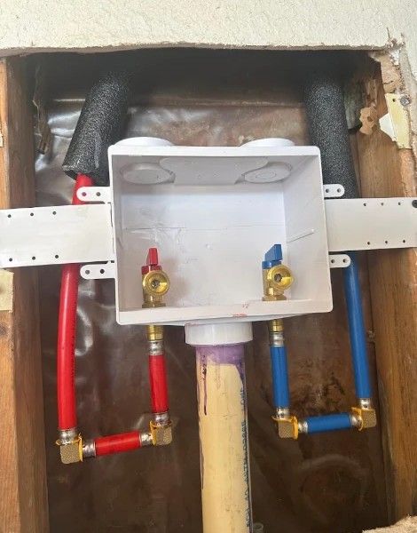 Plumbing rough-in with red and blue water supply valves under a wall-mounted sink box.