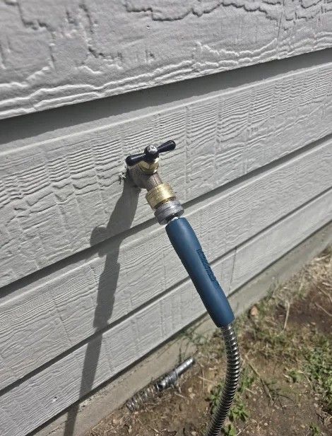 Garden hose connected to an outdoor wall faucet on gray siding