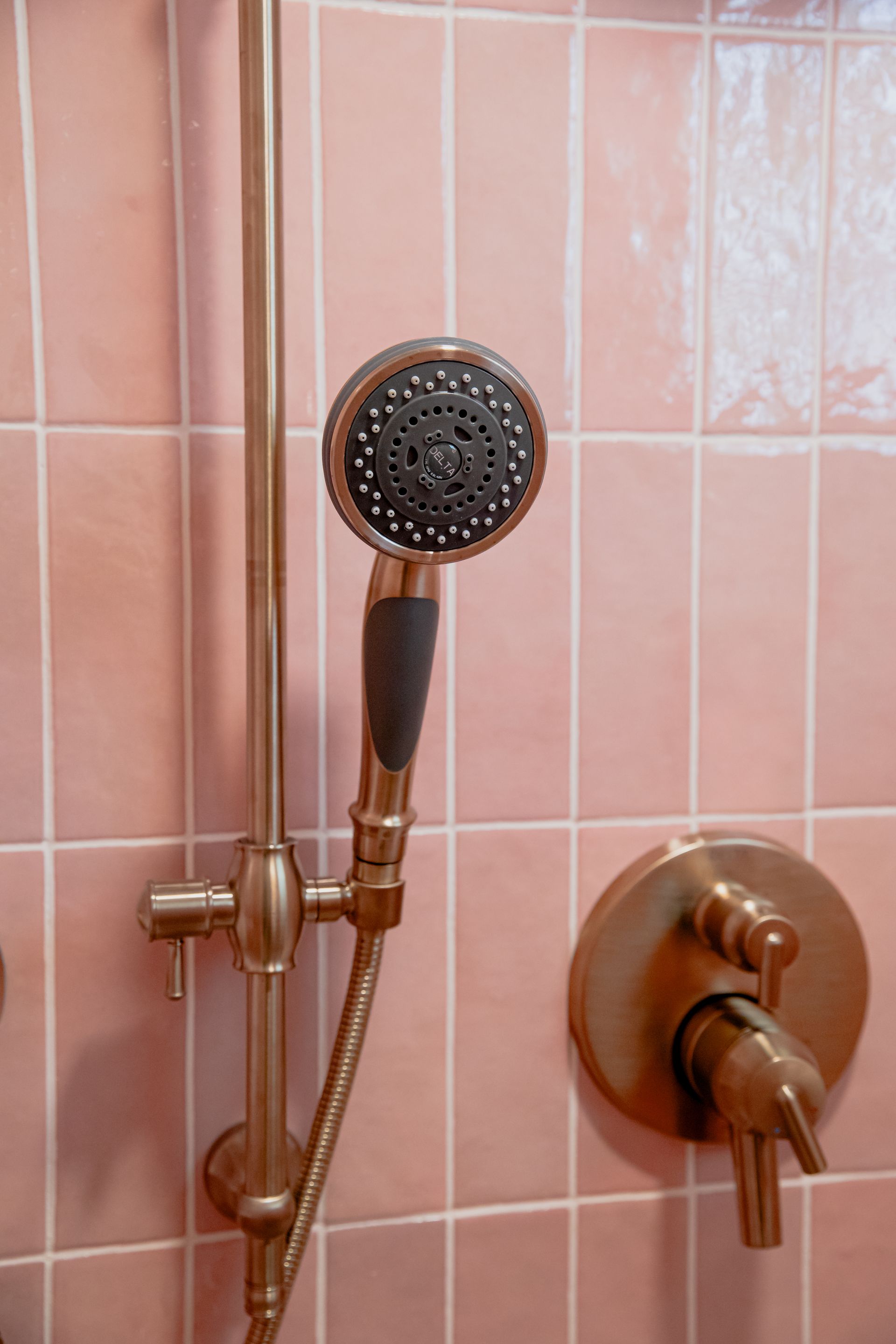 A close up of a shower head in a bathroom with pink tiles.