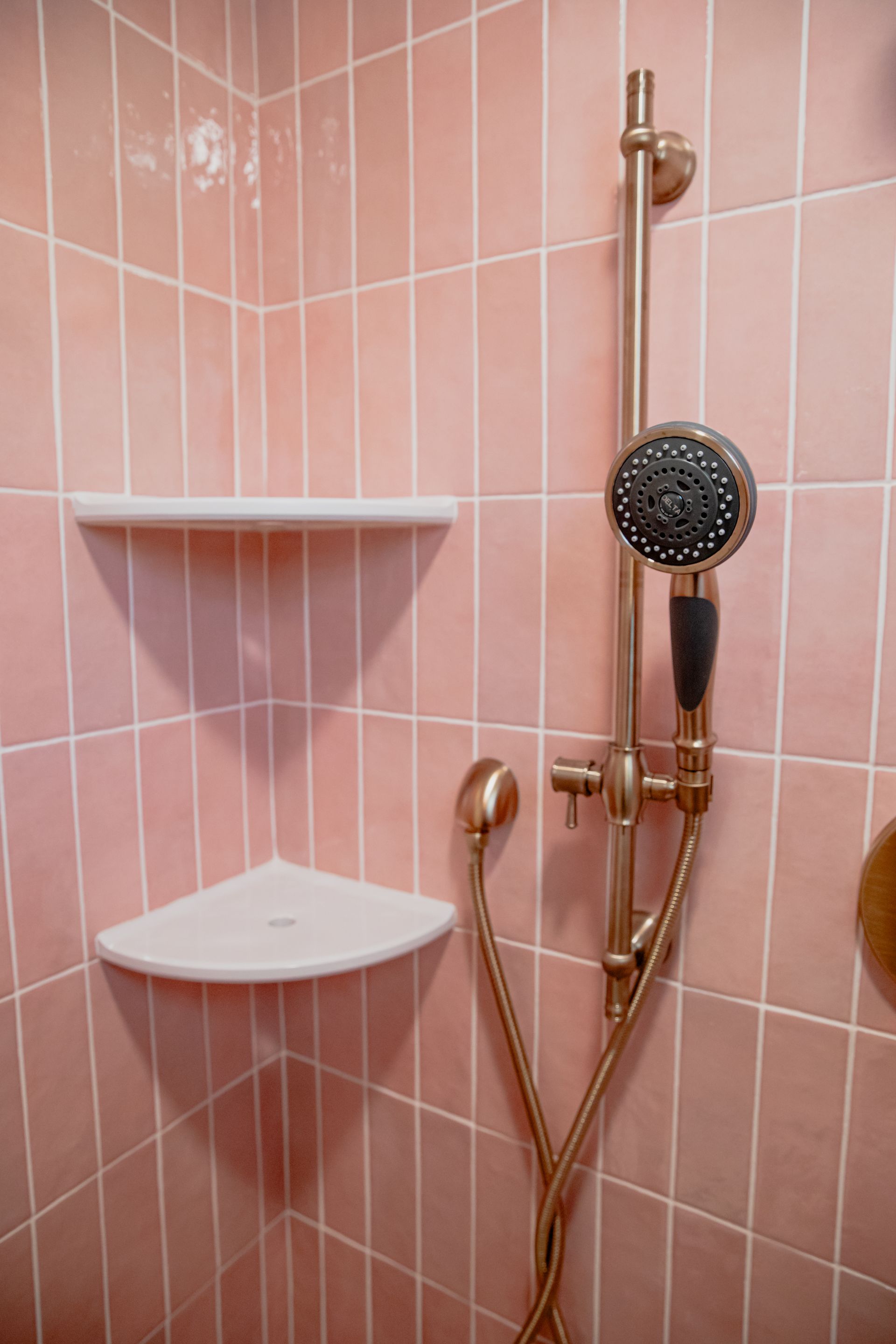 A bathroom with pink tiles and a shower head.