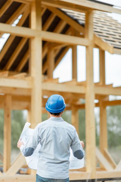 A construction worker is looking at a blueprint of a house under construction.