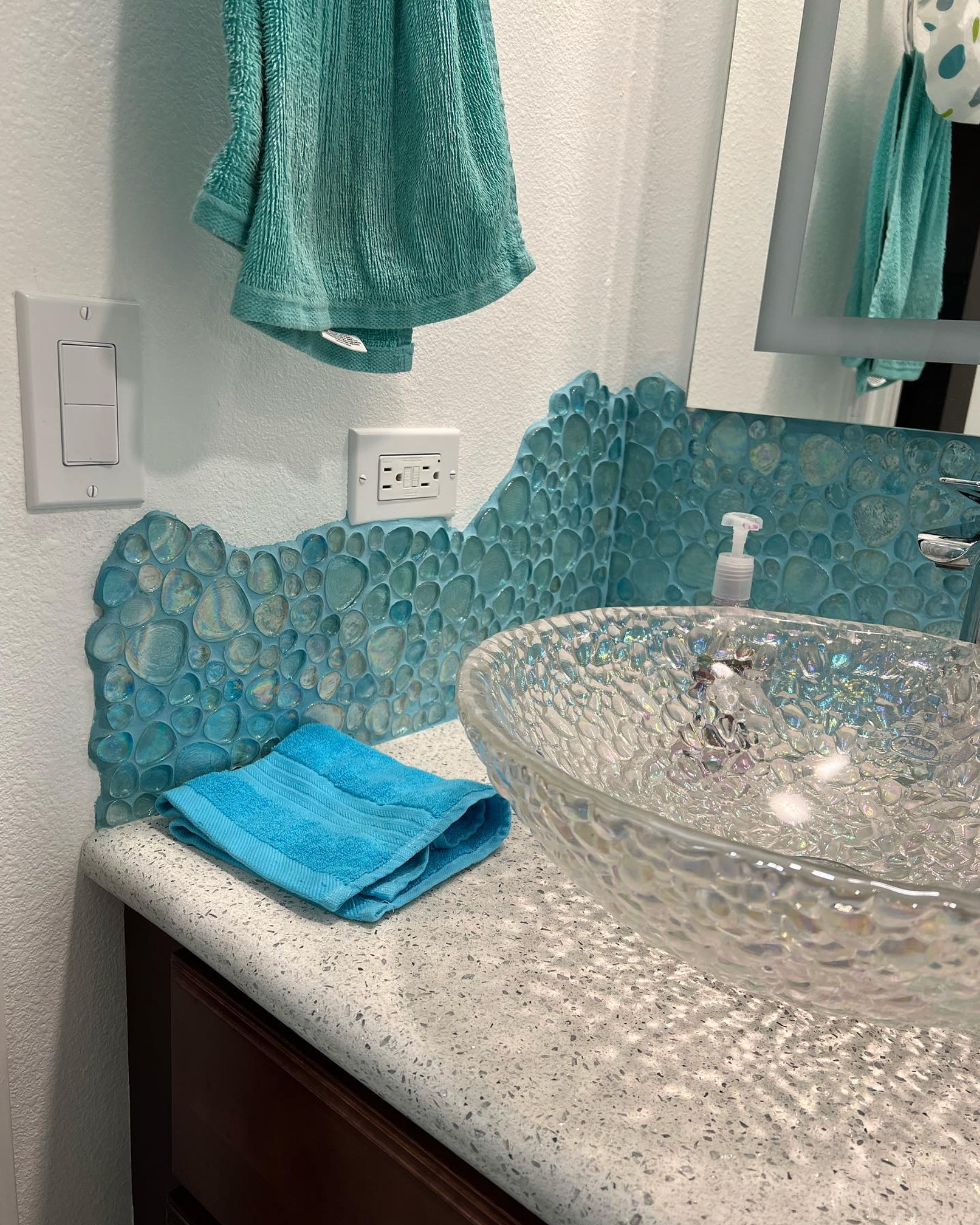 A bathroom with a clear sink and a blue towel on the counter.