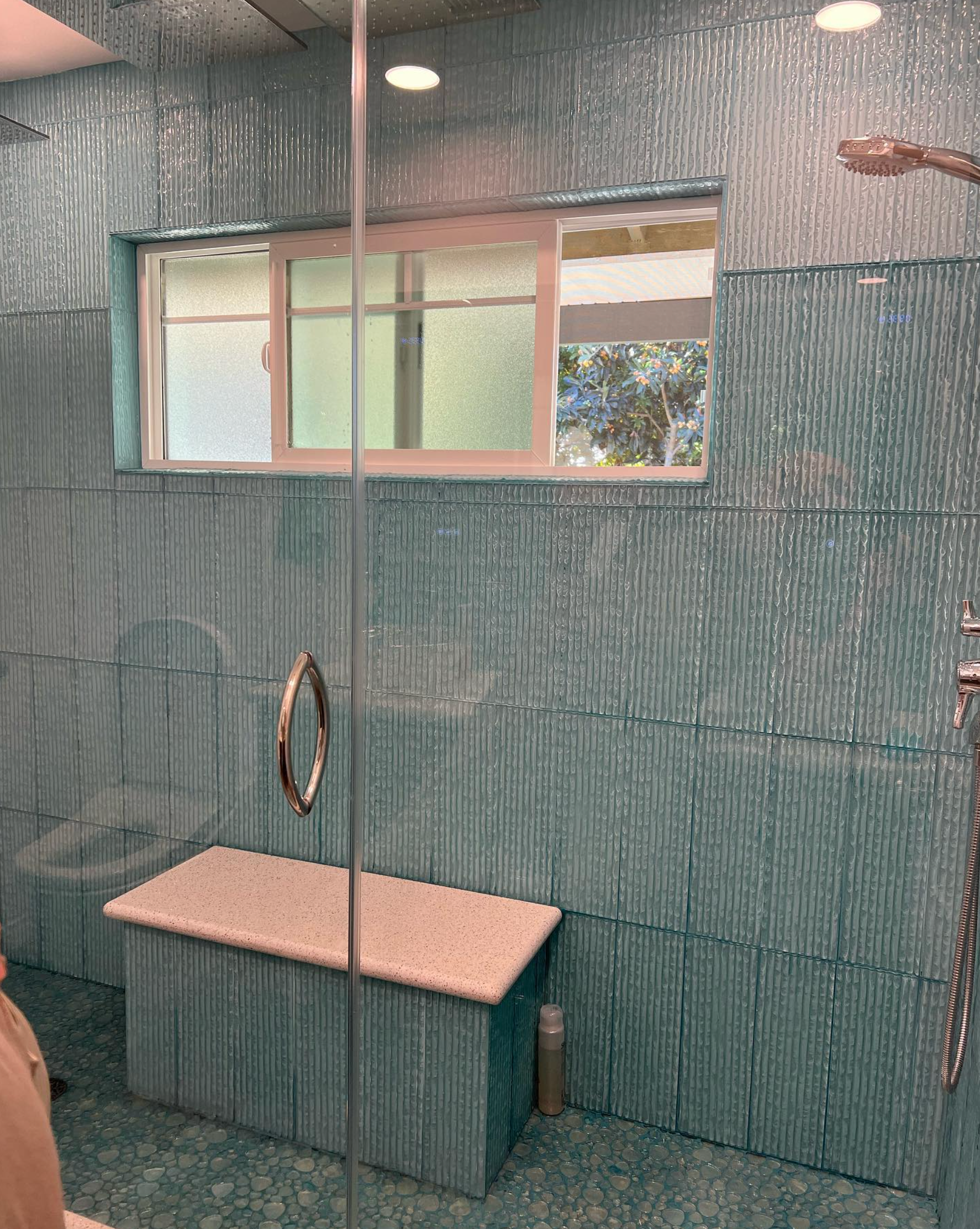 A bathroom with blue tiles and a bench in the shower.