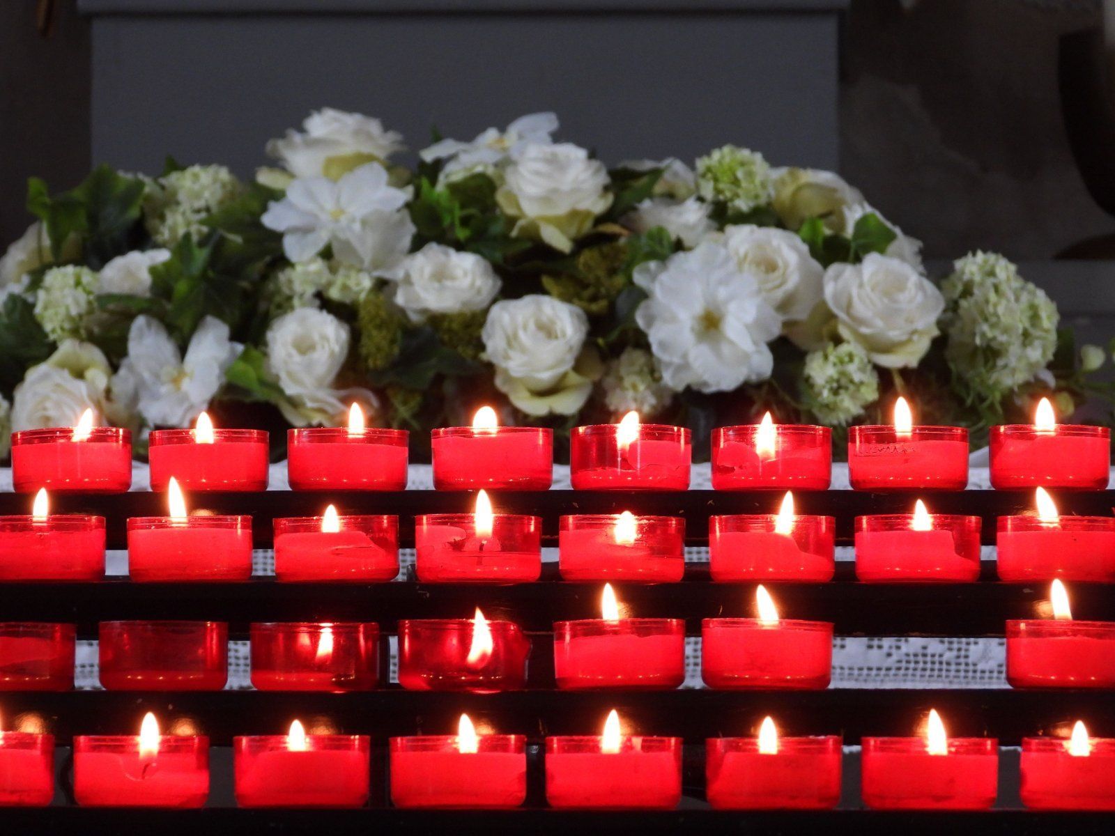 Red memorial candles burning in front of a white floral funeral arrangement during a remembrance service at a Belgium, WI Funeral Home and Cremations.