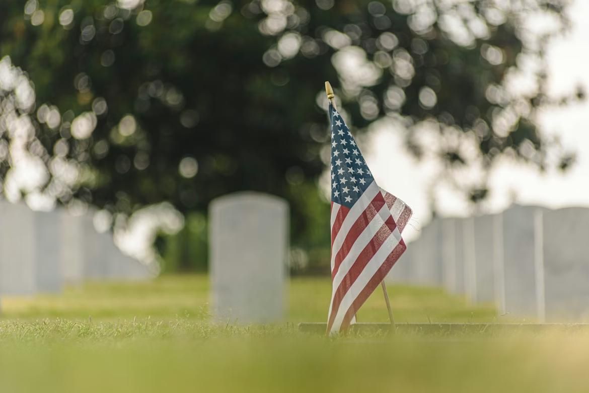 American flag placed beside a gravestone in a cemetery, representing services from a funeral home and cremations Port Washington, WI.