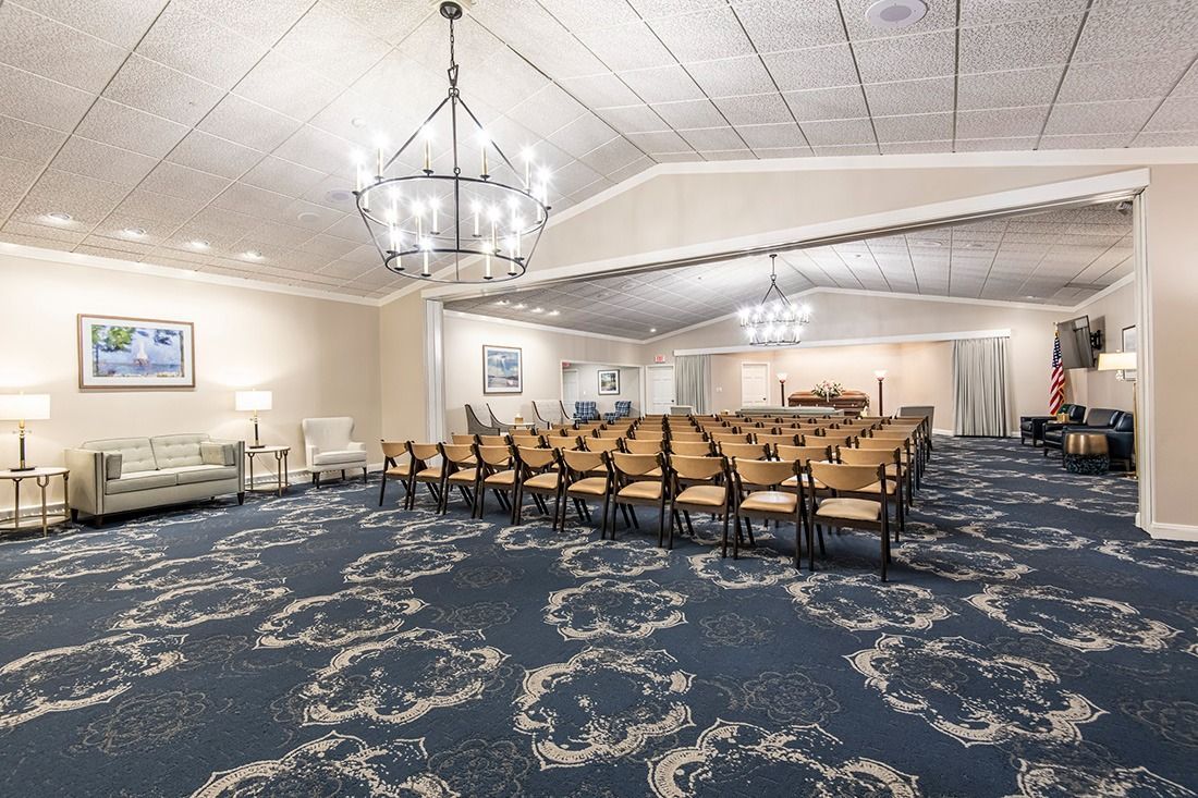 A large, empty chapel with chairs arranged for a service. Blue patterned carpet, cream walls, and chandeliers.