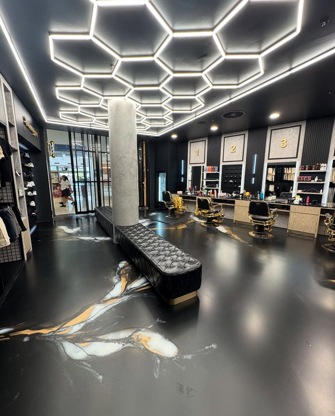 Modern black salon interior with hexagonal ceiling lights, mirrors, styling chairs, and a central bench.