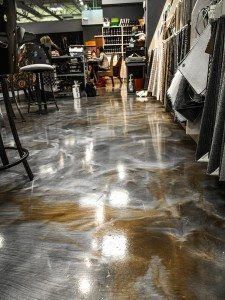 A glossy black floor in a clothing store aisle, reflecting lights and hanging garments.