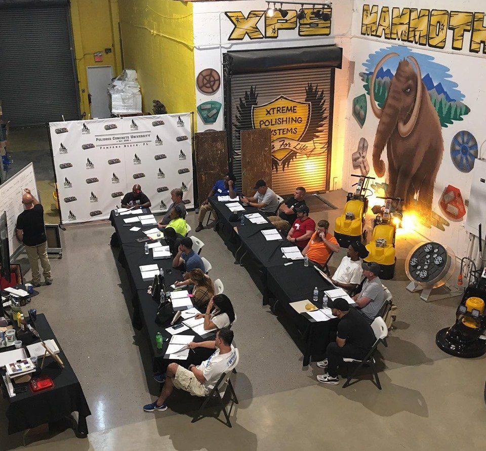 A group of people sit at long tables in front of a wall that says xpe mammoth